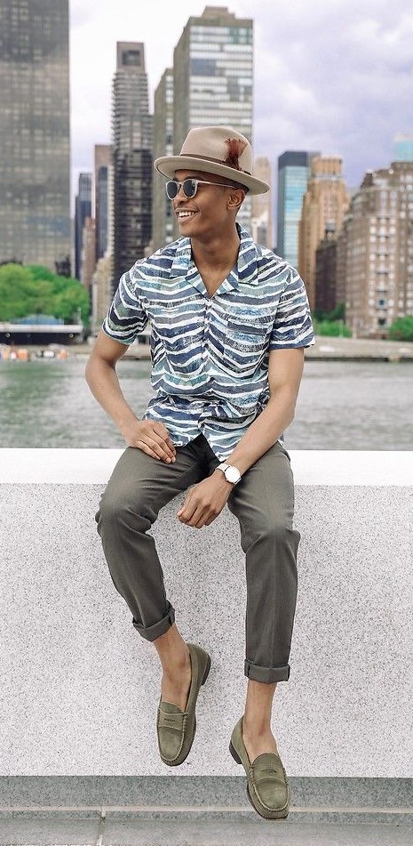 printed shirt with grey trousers accessorized with shades, hat and a watch_