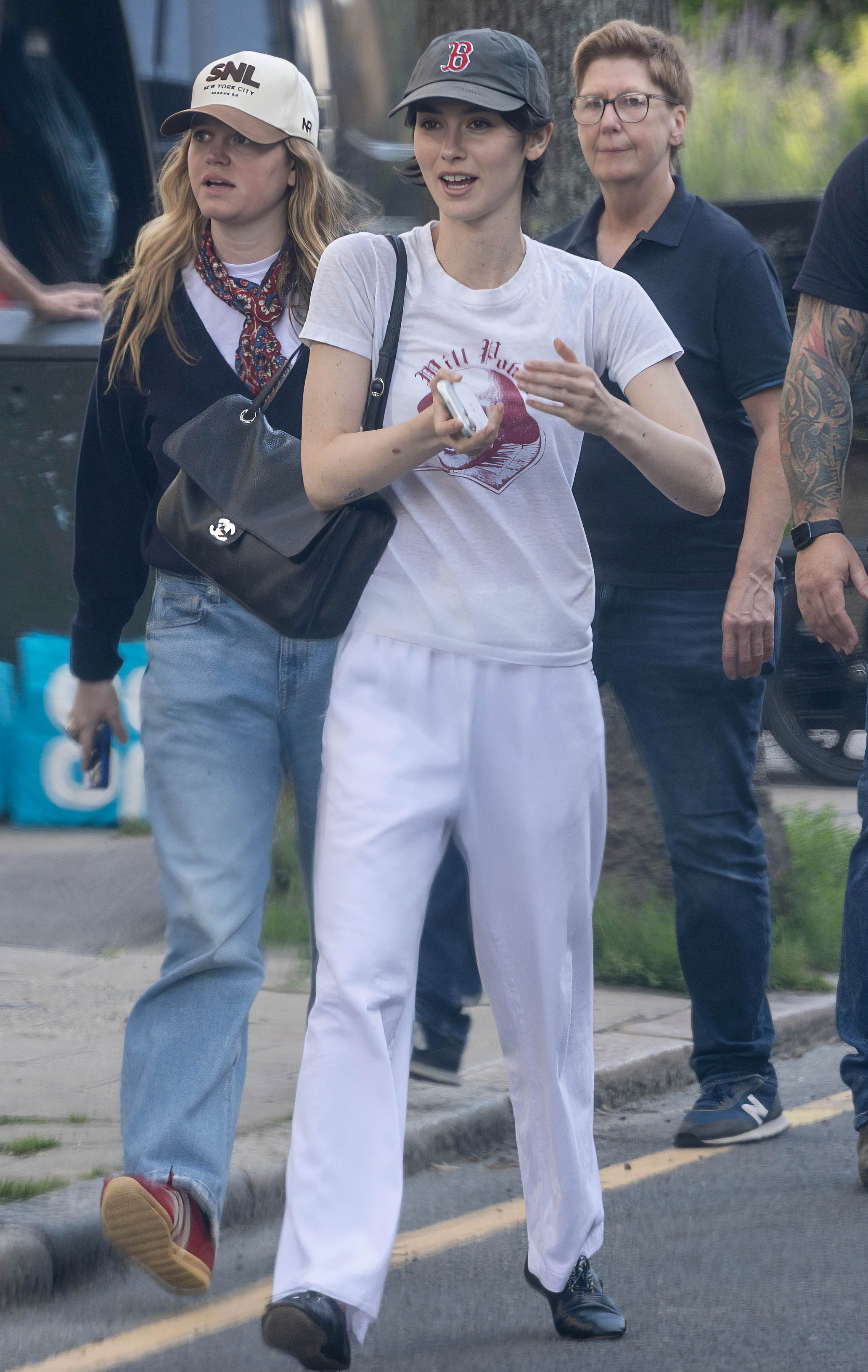 Gracie wears a baseball cap, graphic tee, chanel bag, white pants, and black jazz shoes.