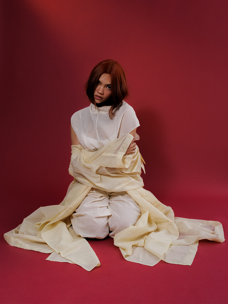 Myra Molloy photographed by David Dickenson. She is in front of a red backdrop wearing a full white look with trench coat by Sportmax.
