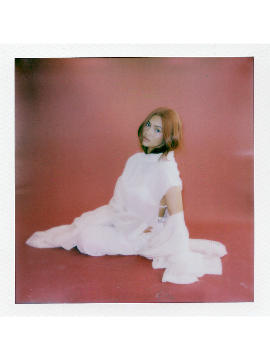 Myra Molloy photographed by David Dickenson. She is in front of a red backdrop wearing a full white look with trench coat by Sportmax.