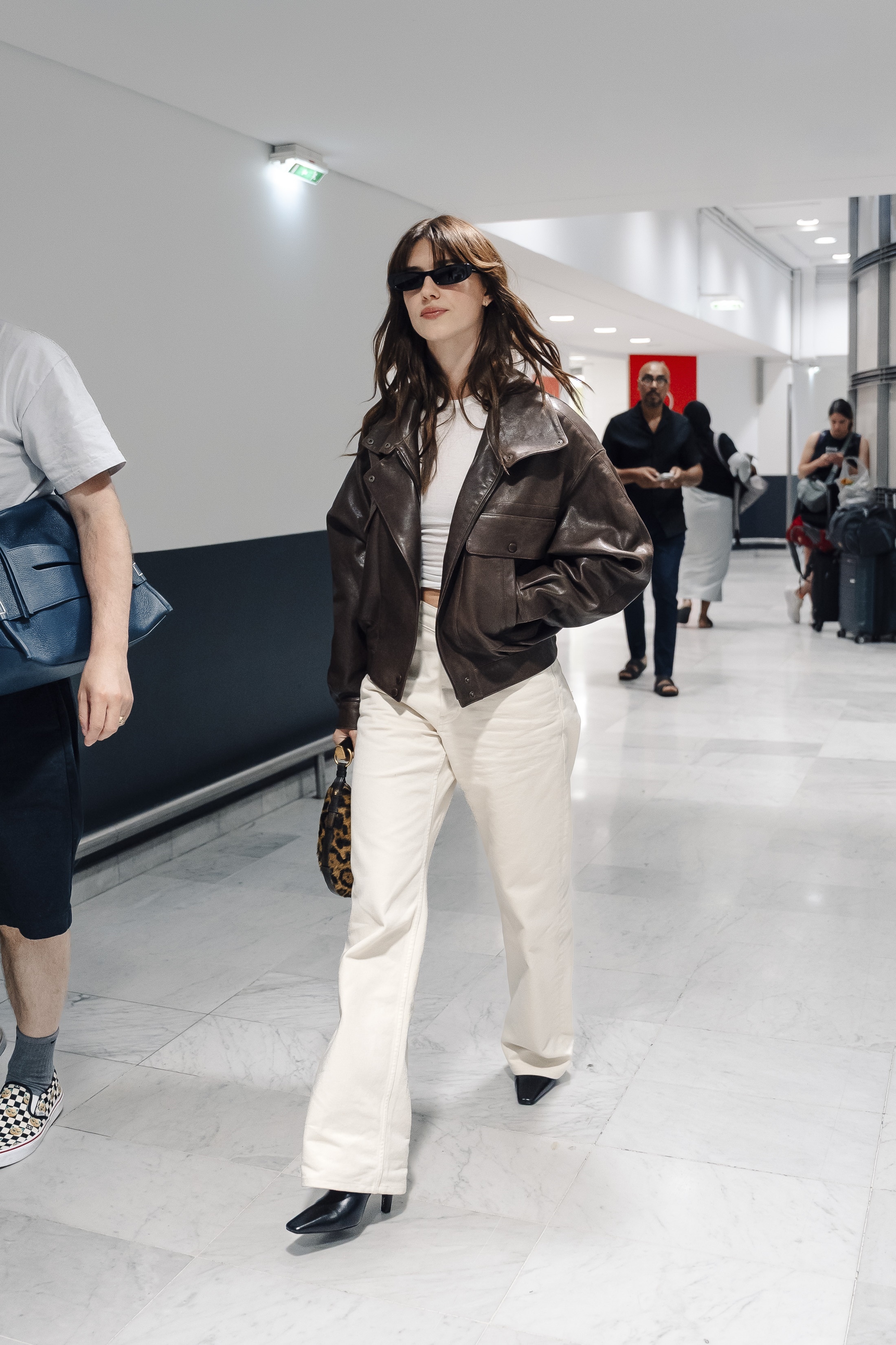 daisy wears a leather jacket, white tee, white jeans, and black heeled boots.