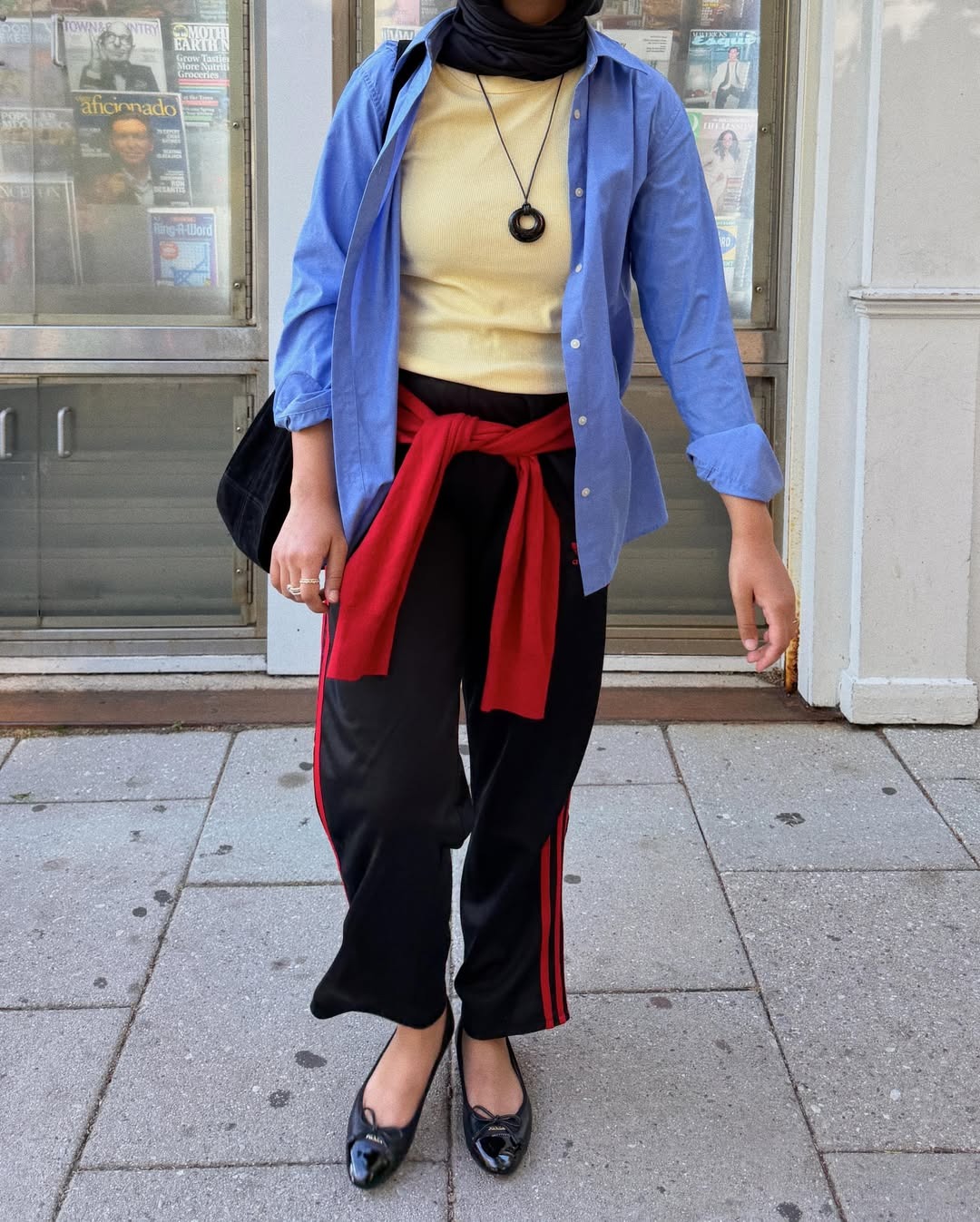NYC woman wears a butter yellow t-shirt, blue button down and track pants with a red sweater tied around her waist and ballet flats.