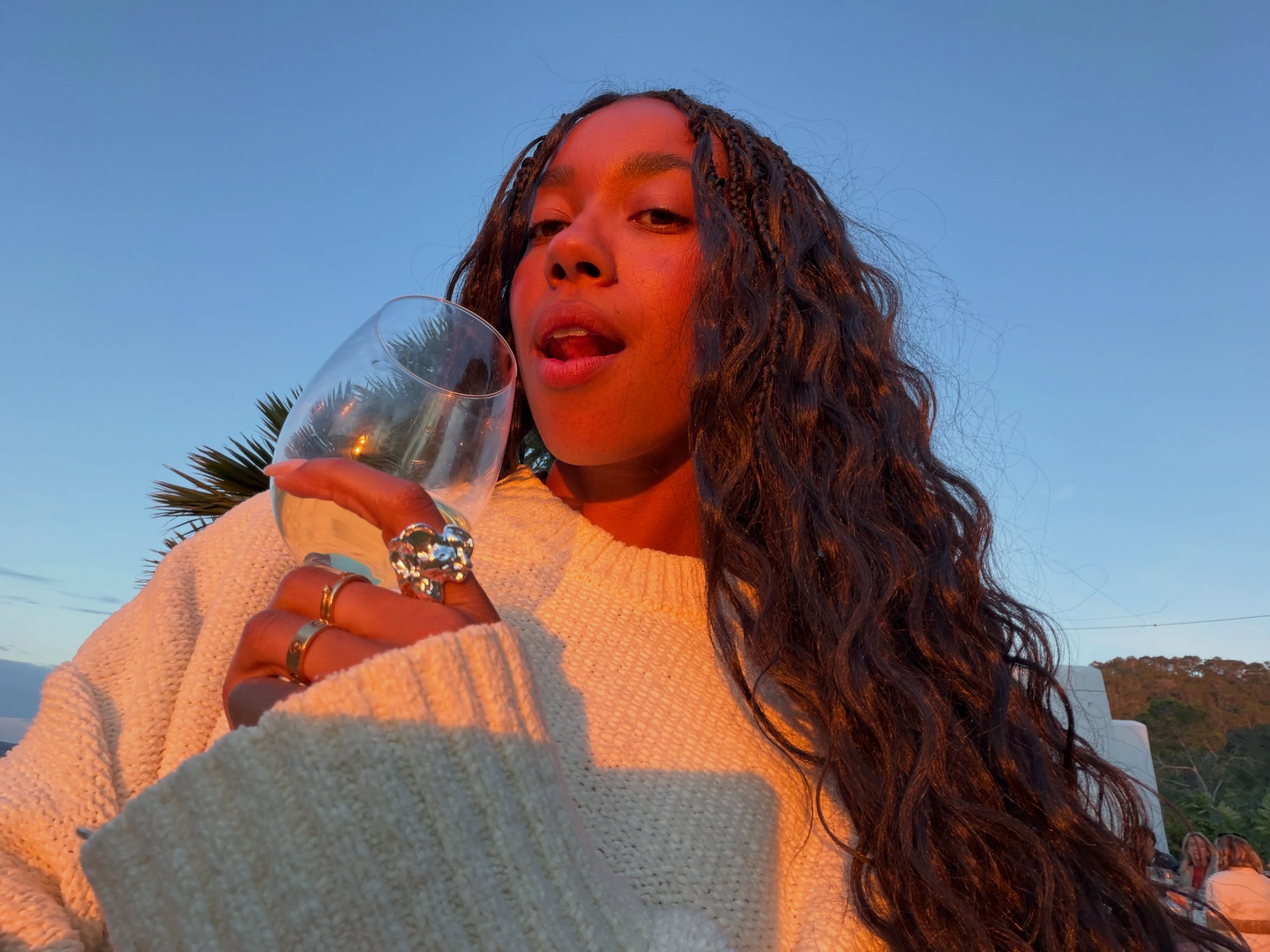 Photo of a woman wearing goddess braids on the beach drinking wine