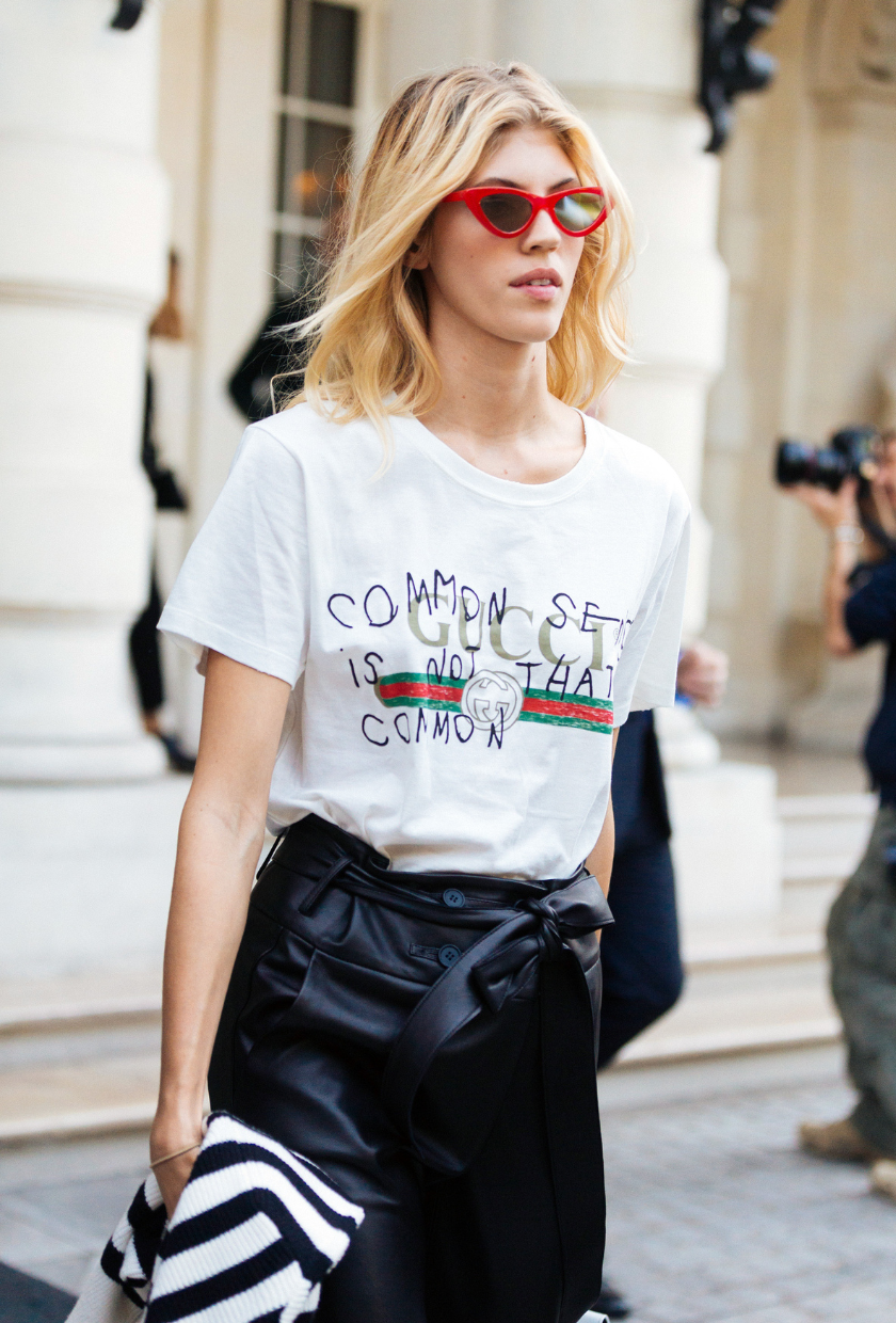 Model Devon Windsor wears red cat-eye sunglasses, a white Gucci logo t-shirt, and black leather skirt during Paris Fashion Week Spring/Summer 2018 on September 29, 2017 in Paris, France.