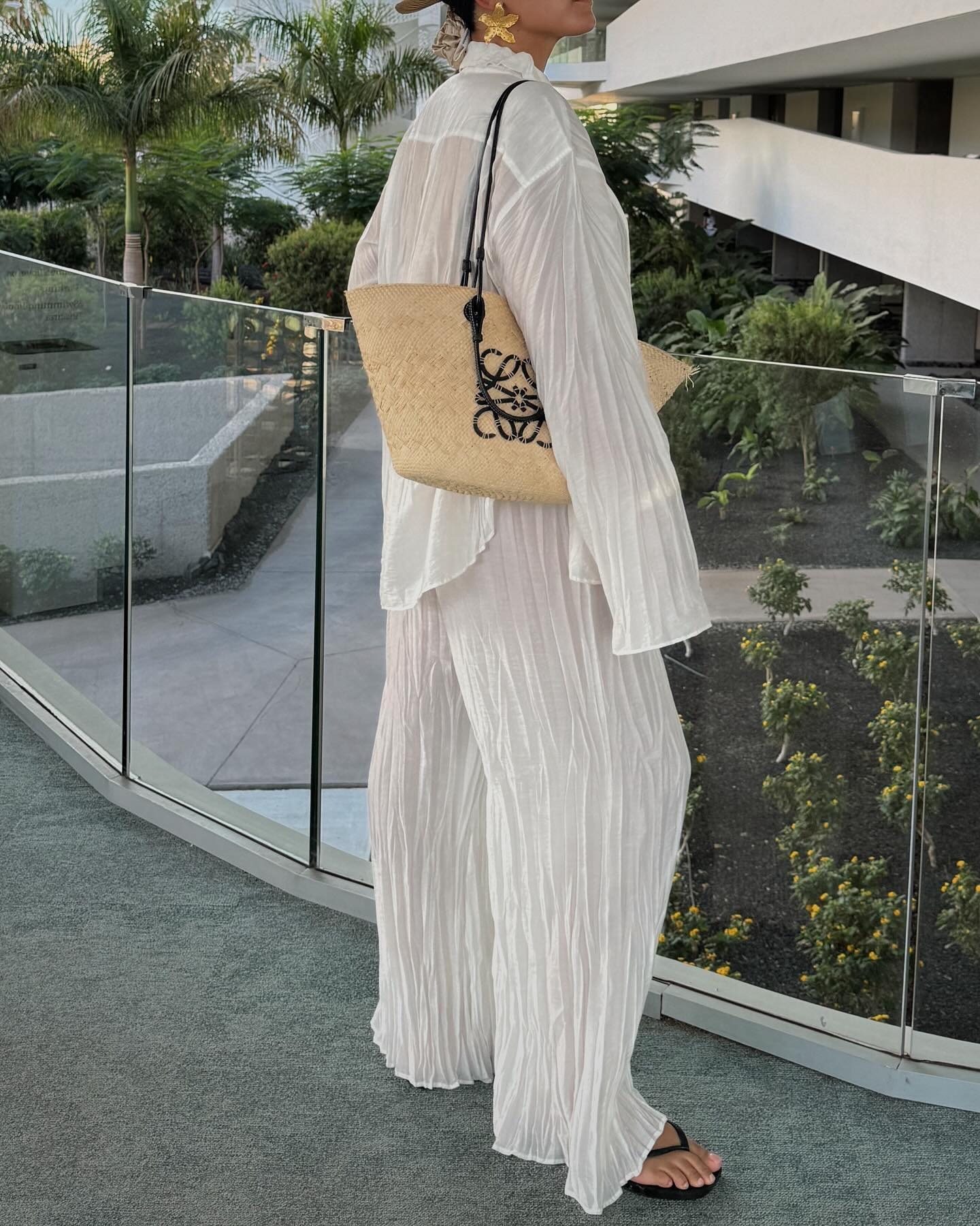 Woman wears white shirred shirt, white shirred trousers, carries Loewe Basket bag