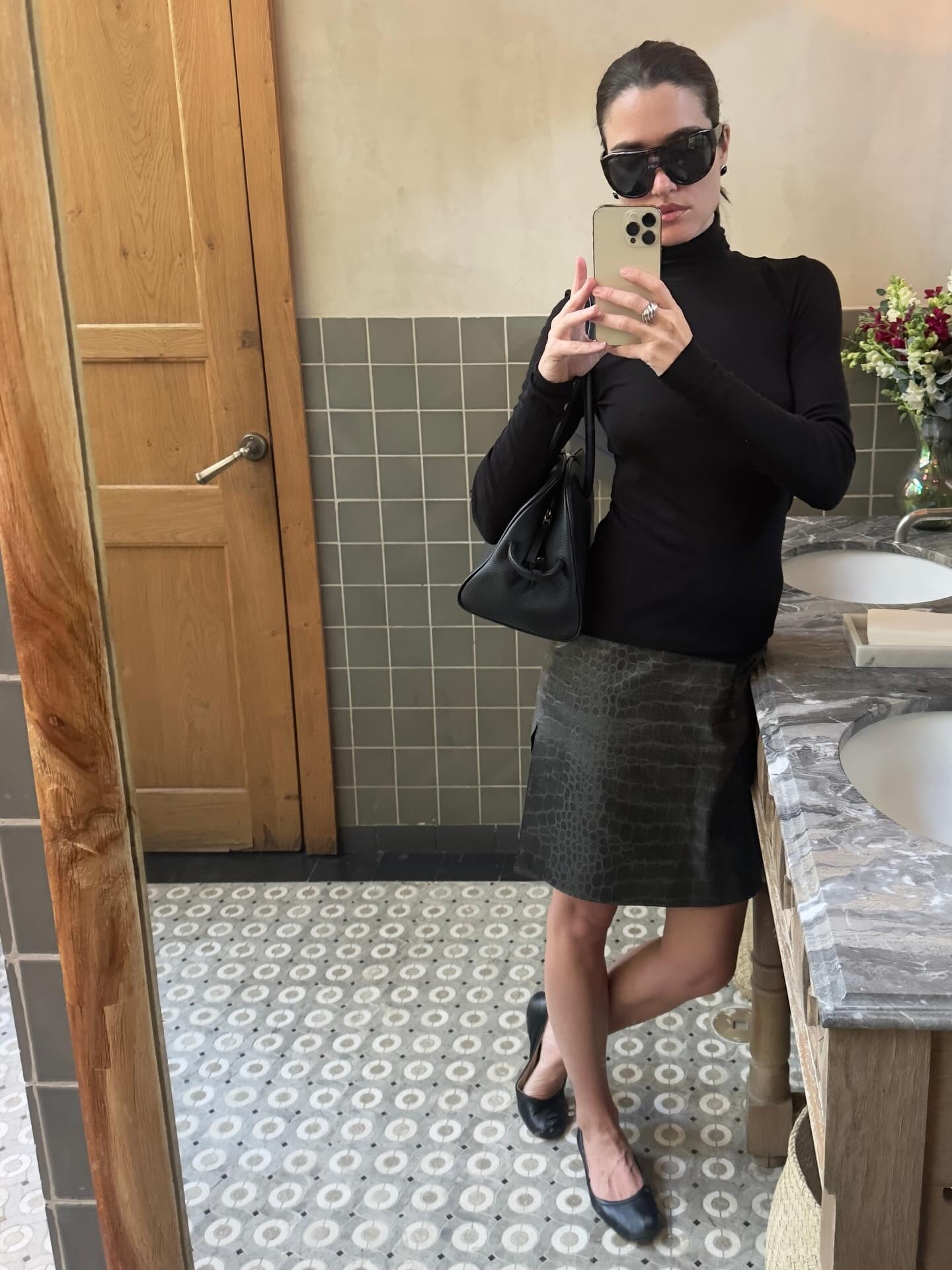 @iliridakrasniqi wearing a black turtleneck and croc knee-length skirt with ballet flats.