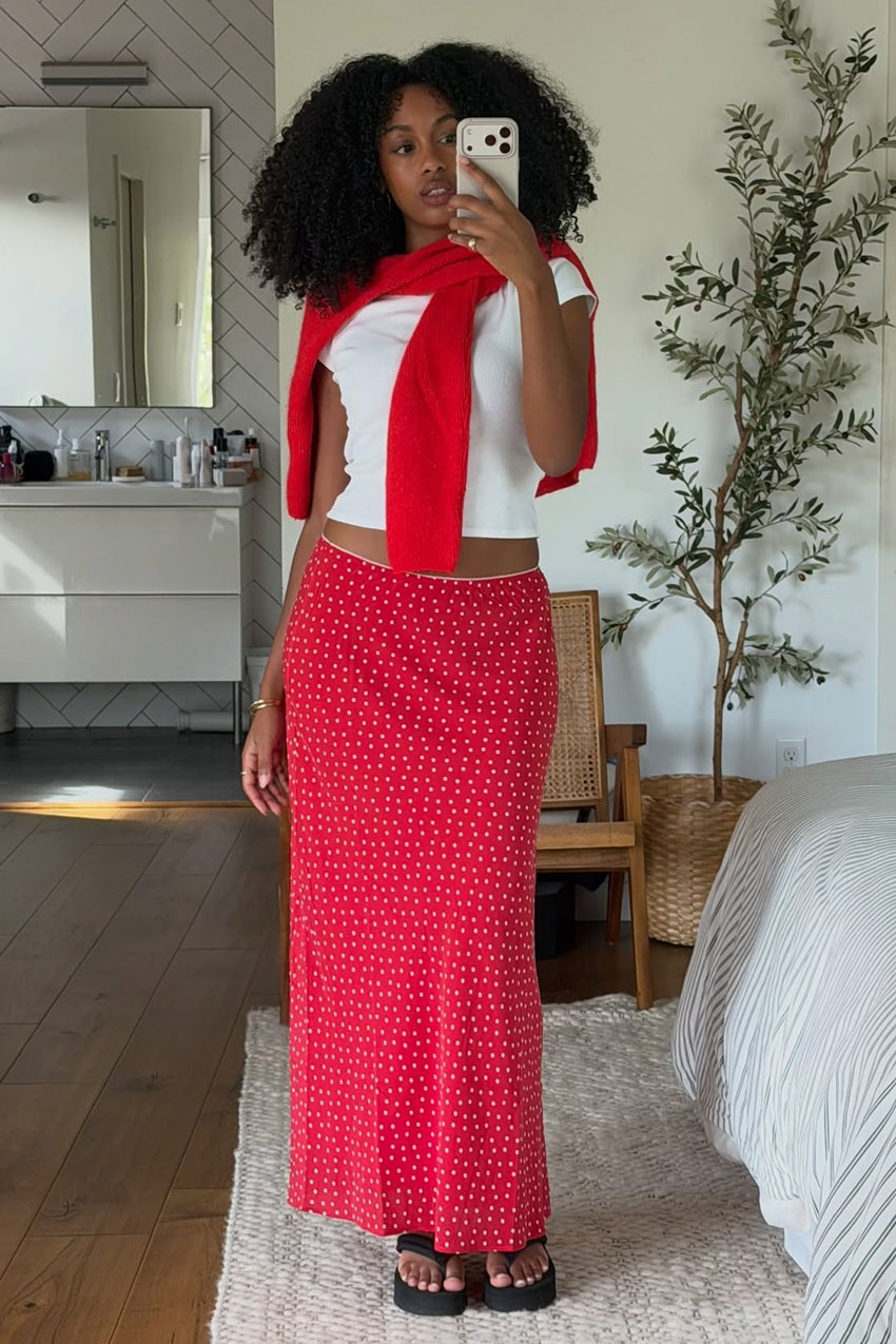 a woman wearing a white tee, red polka dot skirt, black flip-flops, and red cardigan