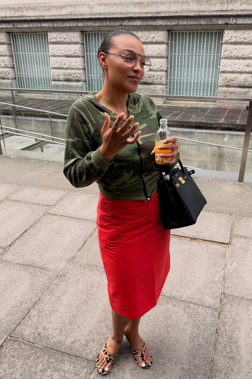 A woman wearing a camo hoodie and red skirt.