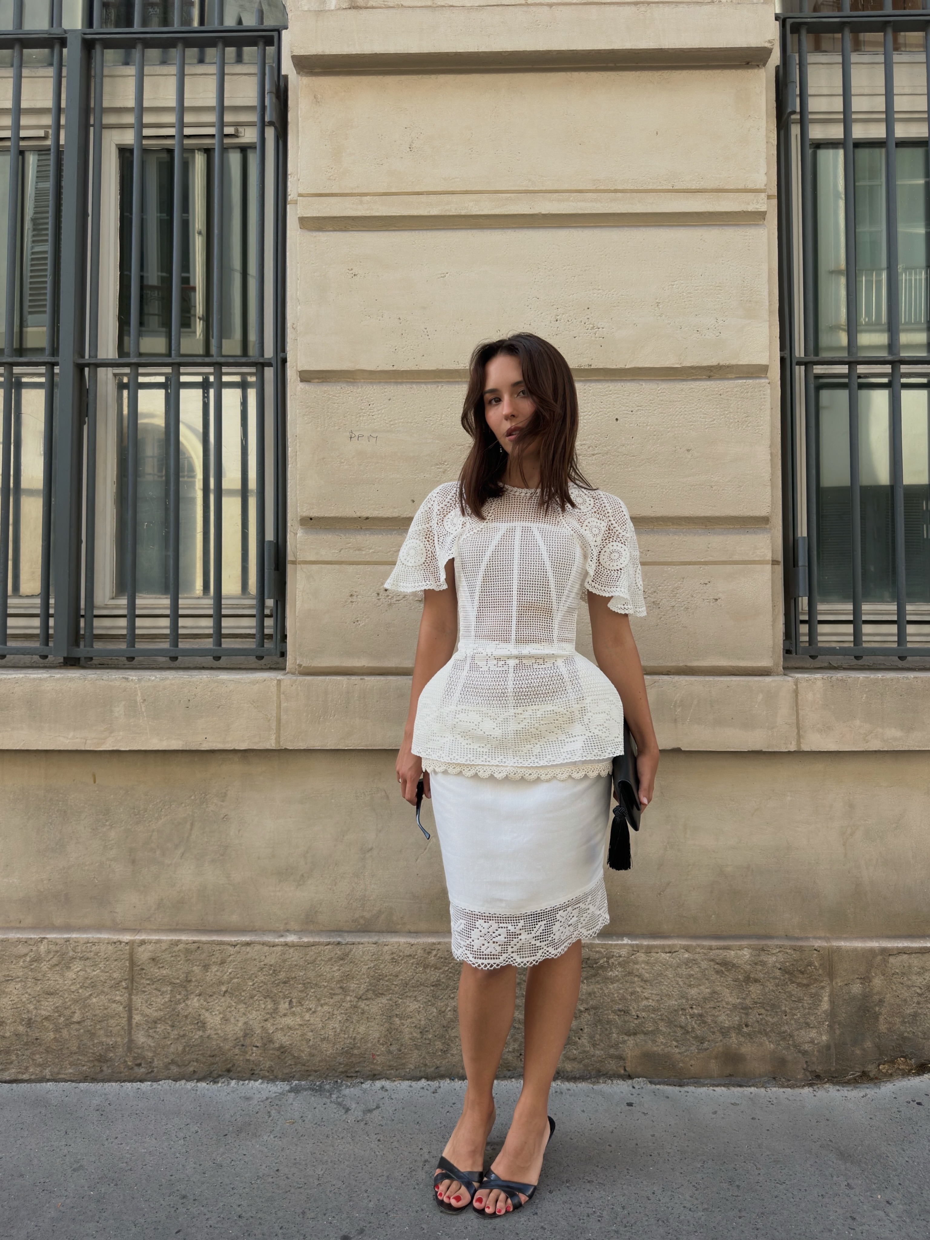 @deborabrosa wearing a white crochet top and skirt with heeled sandals.