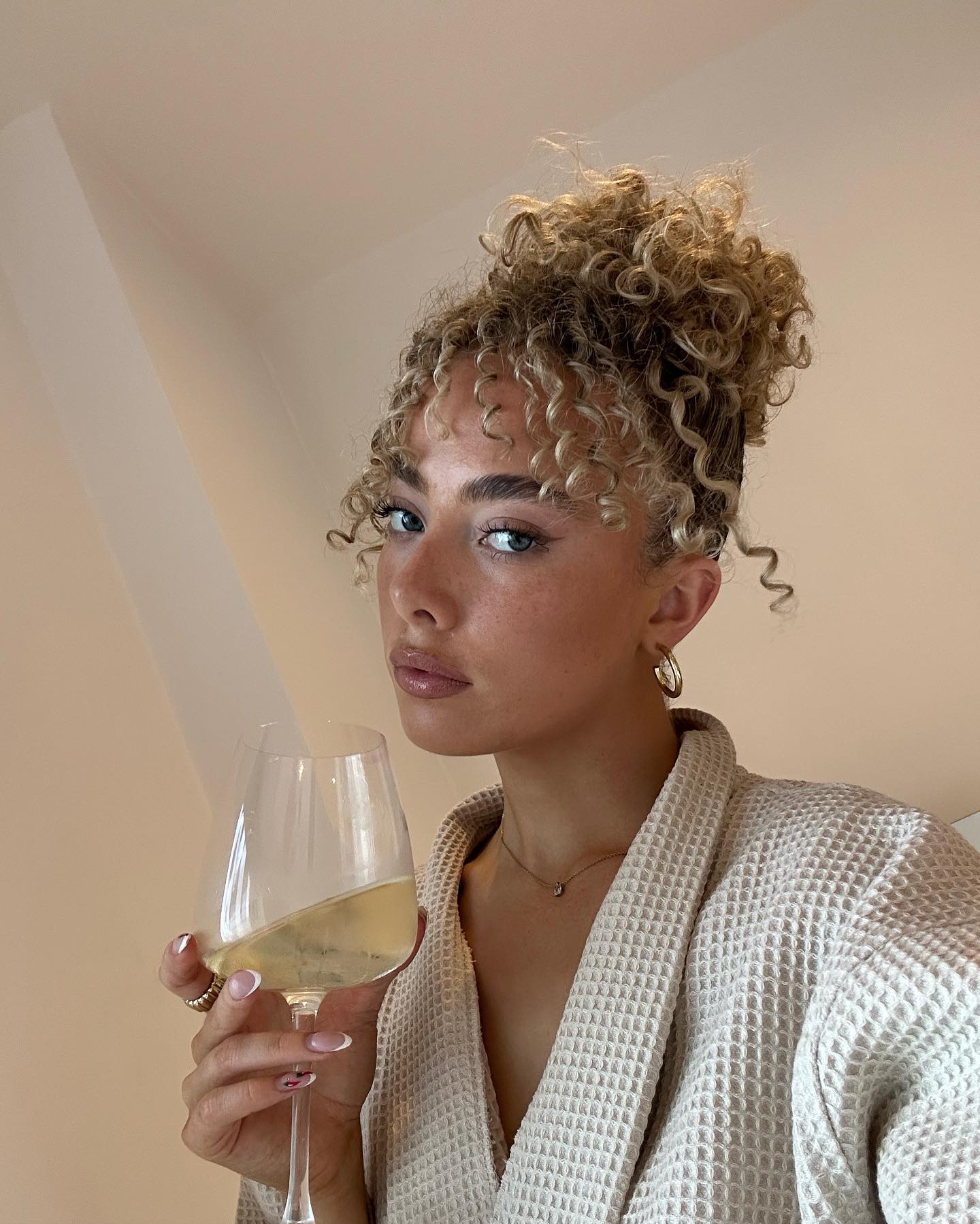 Photo of a woman wearing a curly bun drinking wine in a robe