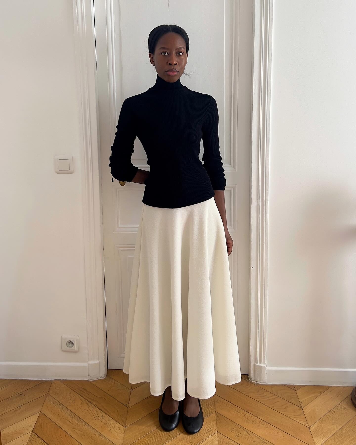 French influencer wearing a black turtleneck and long white skirt with ballet flats