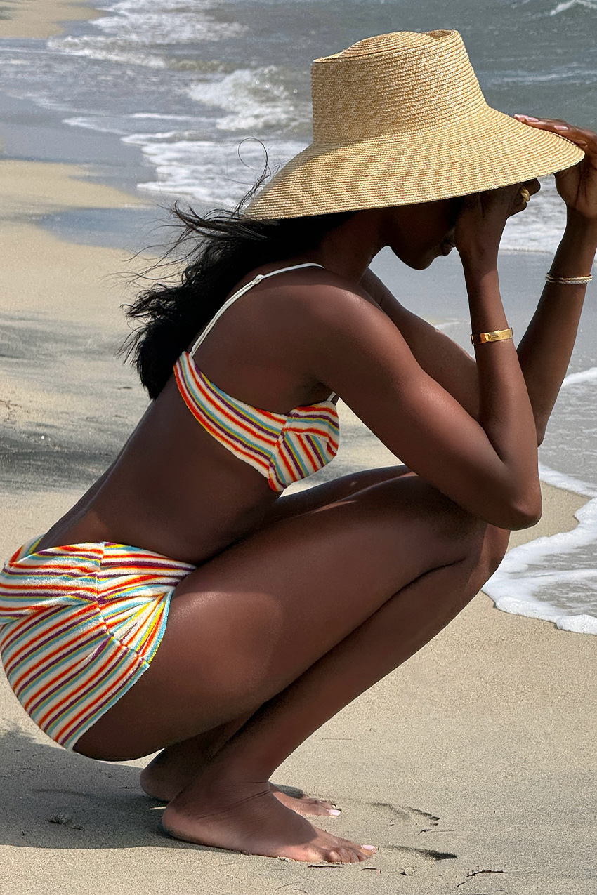 A woman wearing a striped bikini top styled with matching retro swim shorts and a raffia hat at the beach.