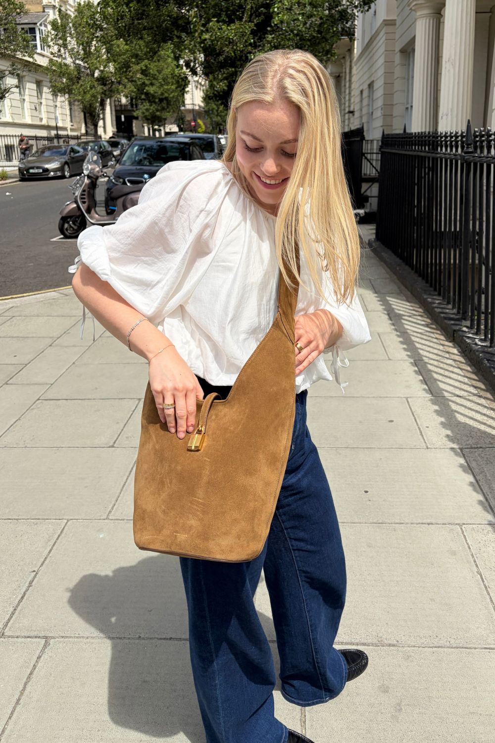Woman wears white blouse, blue jeans, brown suede bag