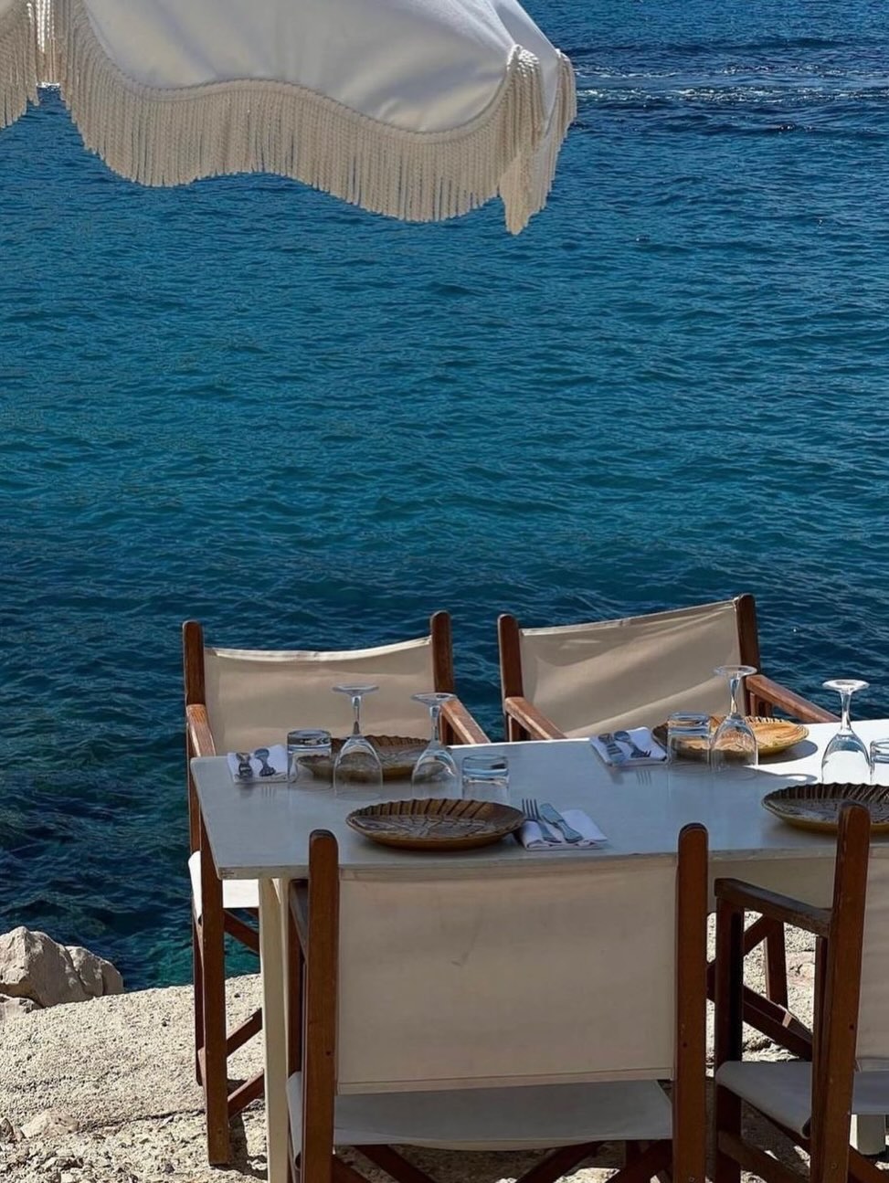 A table setting under an umbrella on the Mediterranean Sea.