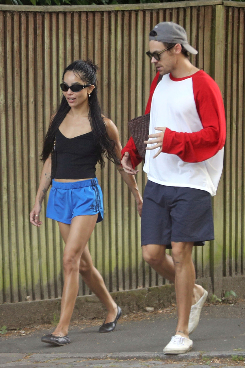 Zoe Kravitz wearing black sunglasses, a black tank top, blue shorts, and black flats