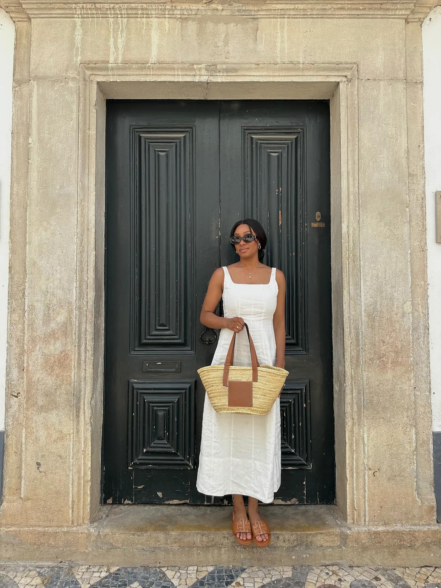 Woman wears white dress, brown sandals and carries woven basket bag
