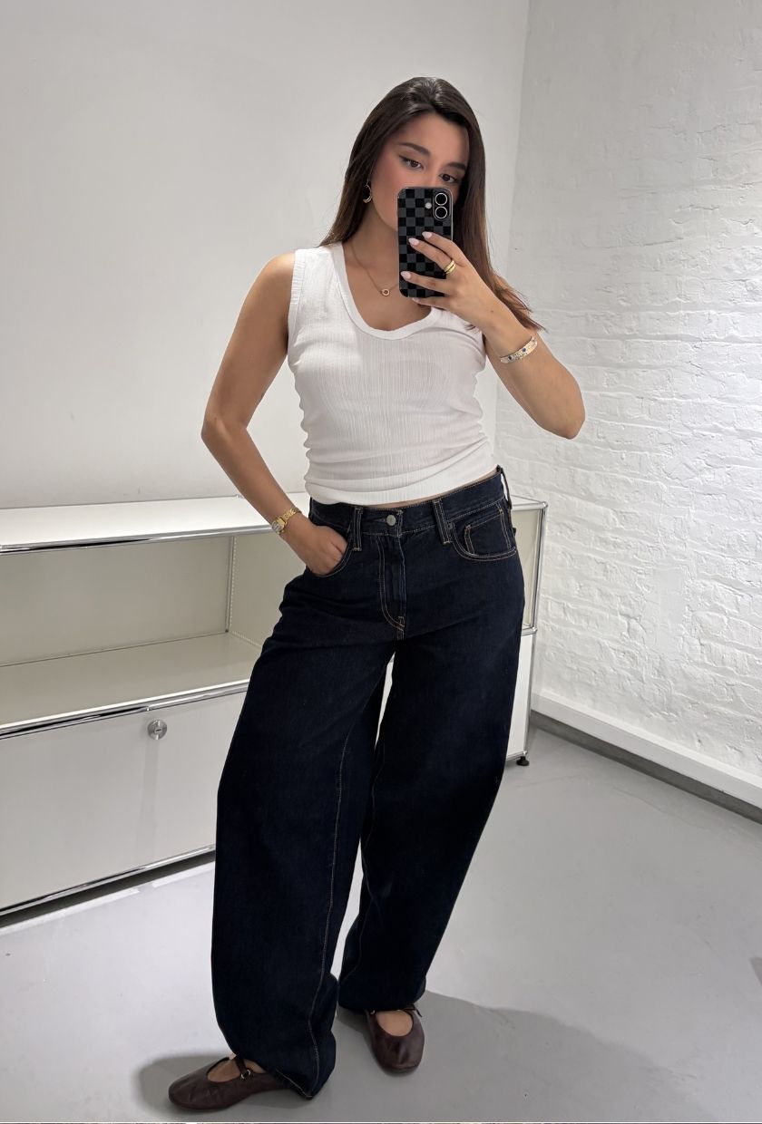 Woman wears white tank top, blue jeans