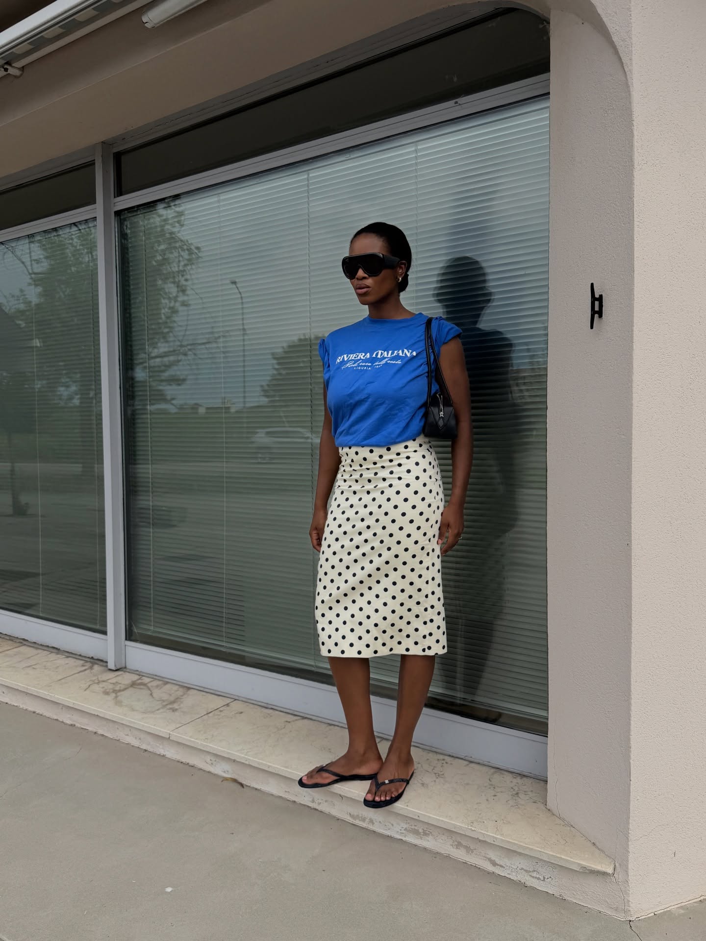 Influencer Marilyn NK wearing a blue graphic t-short, polkadot skirt, thong sandals and shoulder bag.