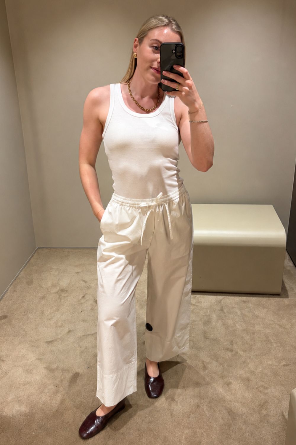 Woman wears white tank top , white jeans and burgundy ballet flats