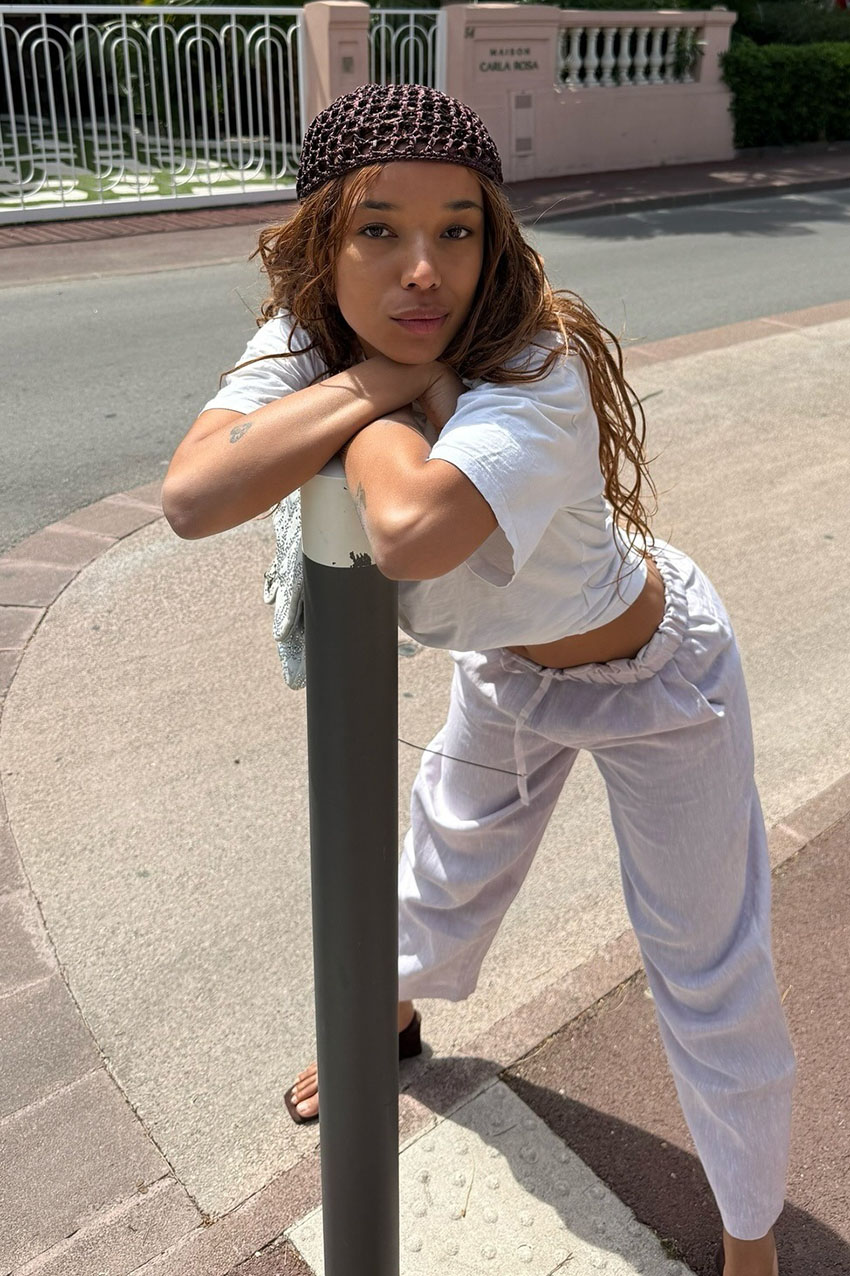 a woman wearing a white t-shirt, white pants, and a brown crochet cap