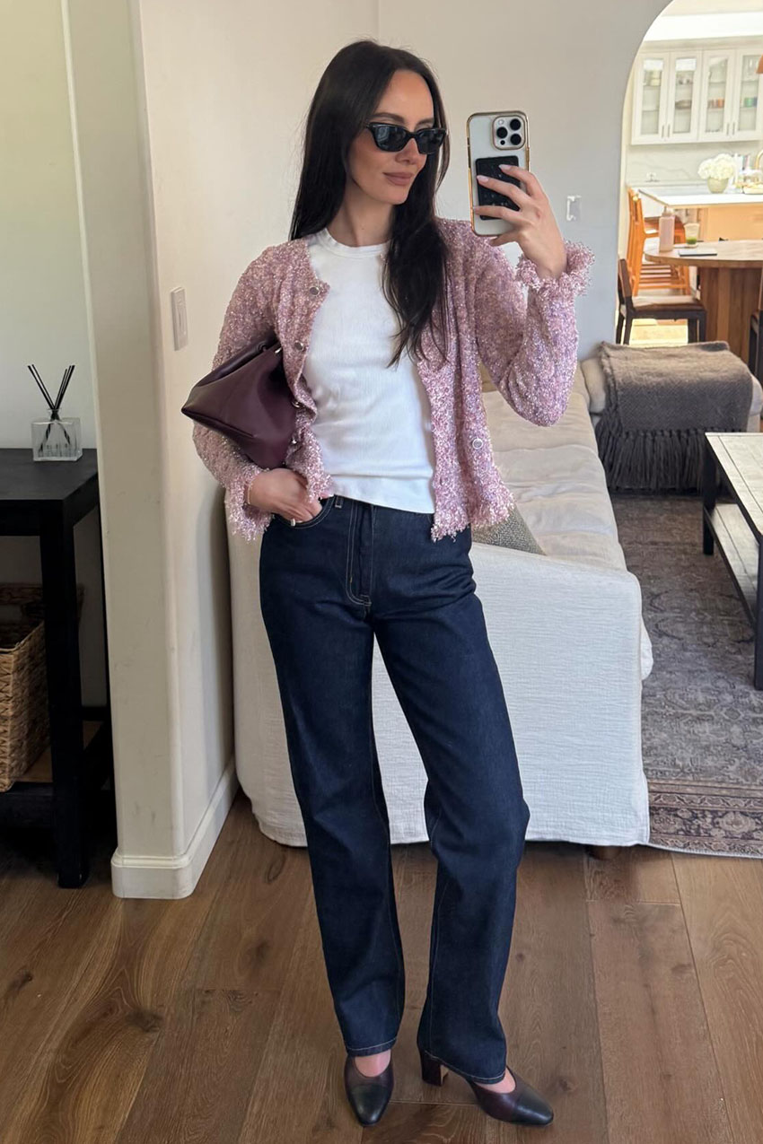 a woman wearing a pink cardigan, white tee, blue jeans, and black heels