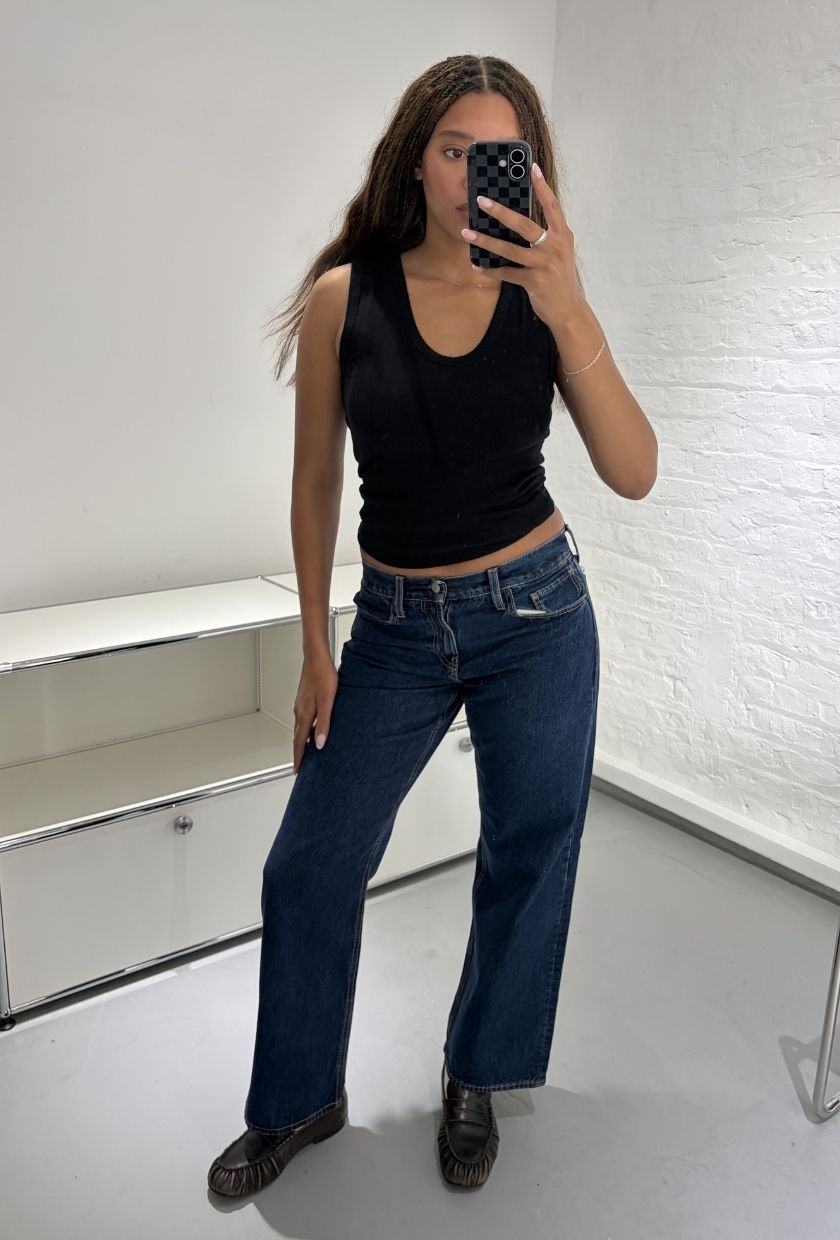 Woman wears black vest top, blue jeans and black loafers