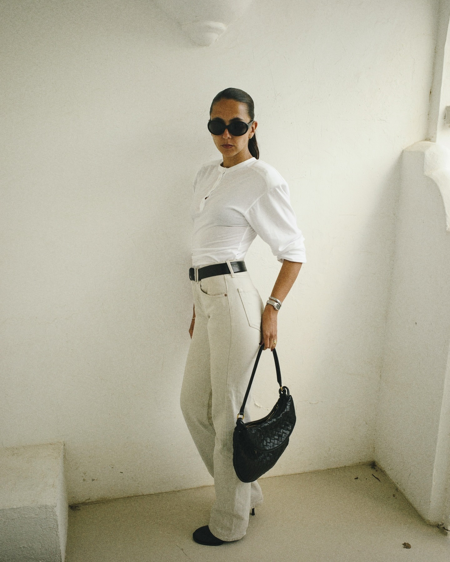 hanna wears a white tee, black belt, white jeans, black boots and a black bag.