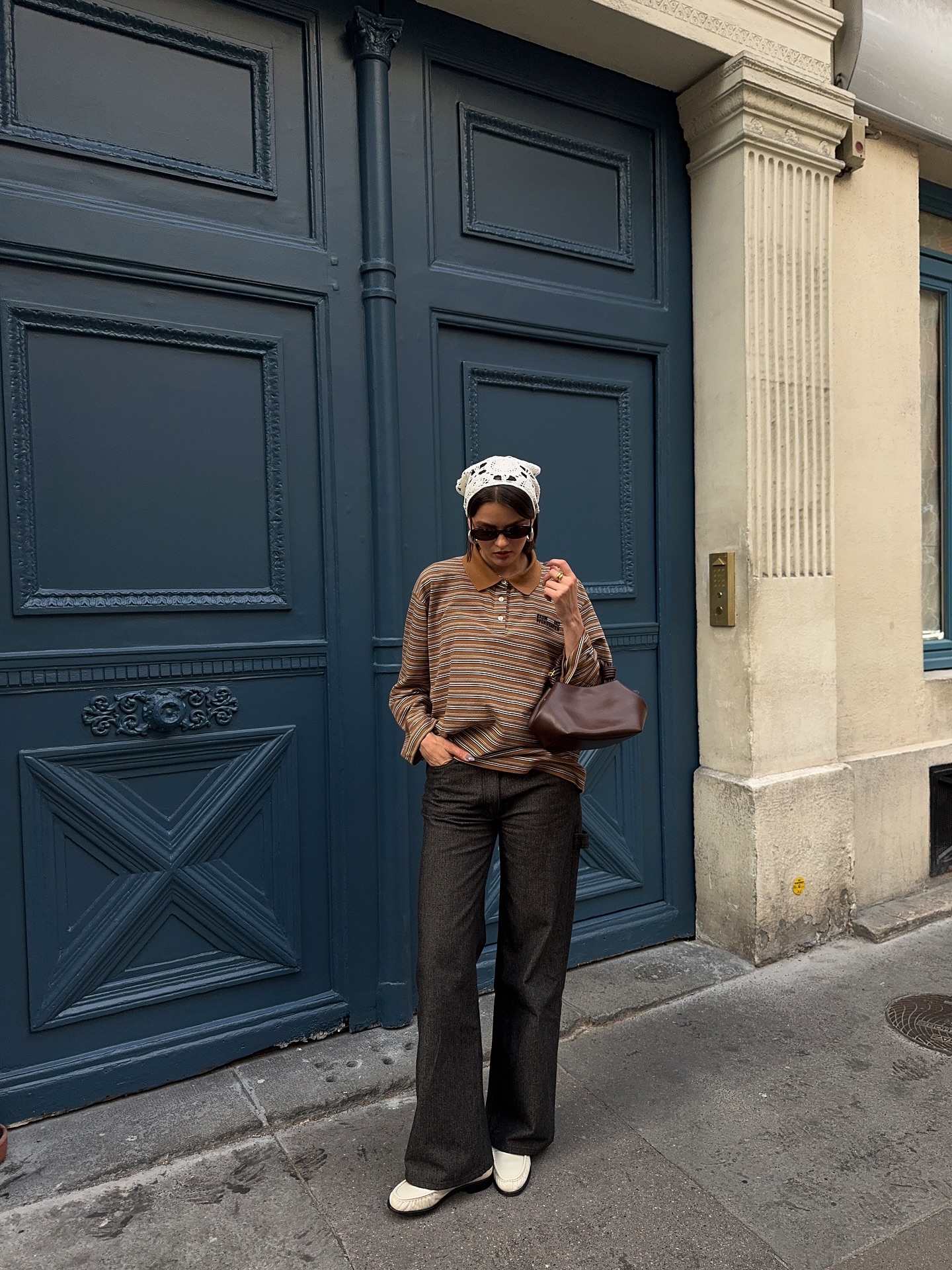 An image of an influencer in dark-wash jeans, a striped long-sleeved top, white loafers and a lace bandana worn around her head in Copenhagen