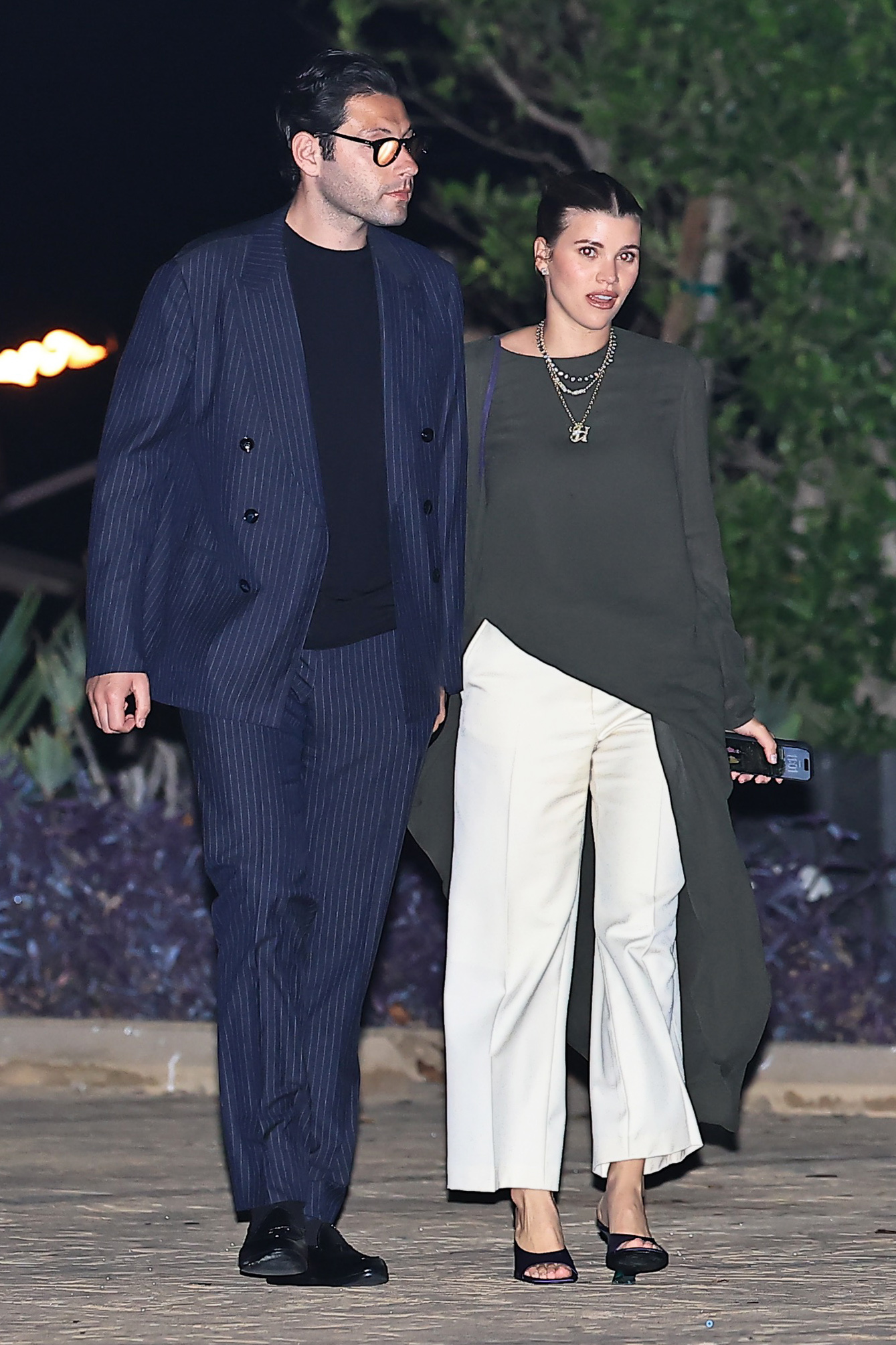 Sofia Richie and Elliot Grainge at Nobu Malibu, and she's wearing an asymmetrical long-sleeve gray top with wide-leg white pants and purple satin Dries Van Noten wedge mules