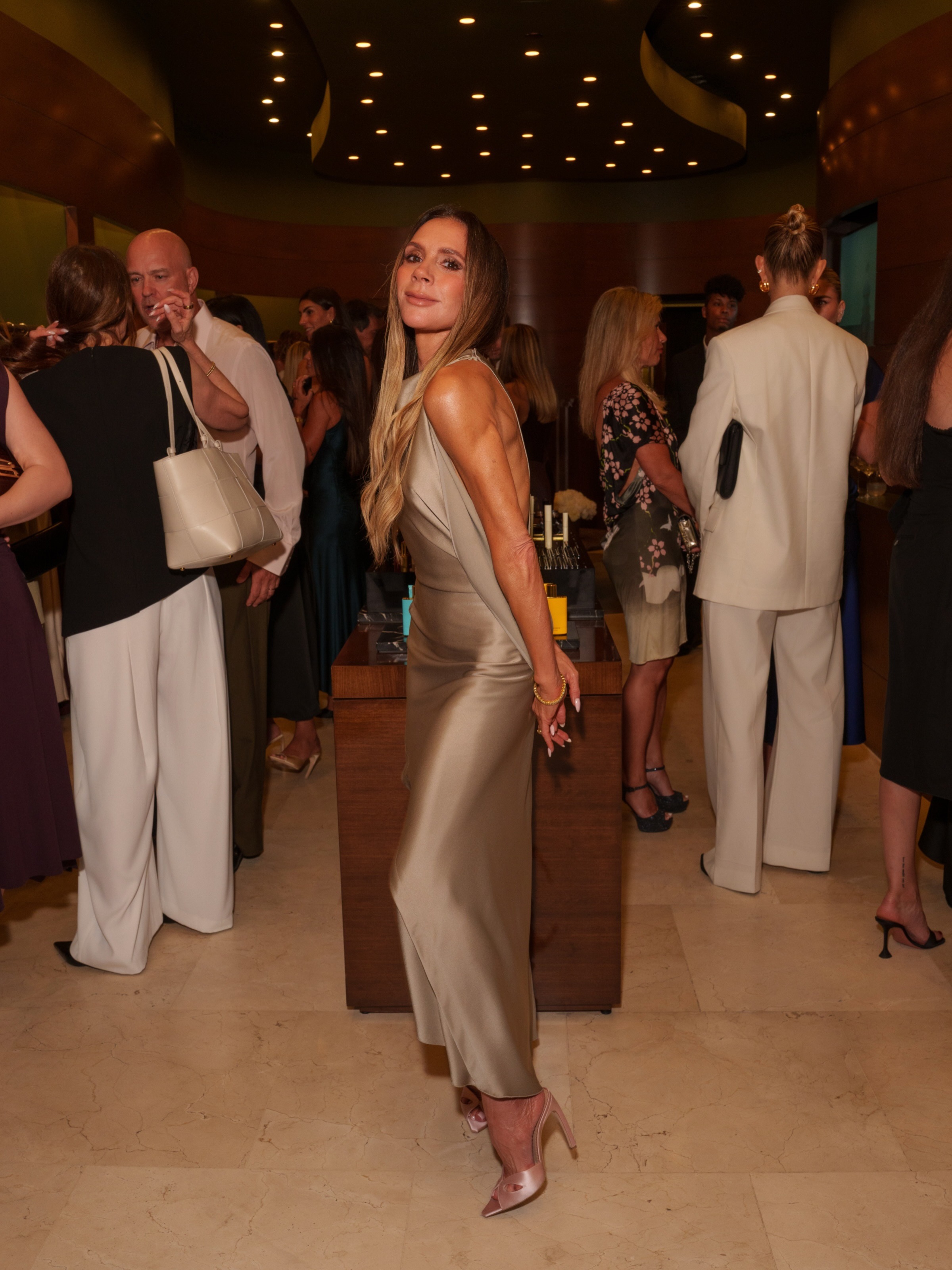 Victoria Beckham wears a neutral dress with pink satin heels.