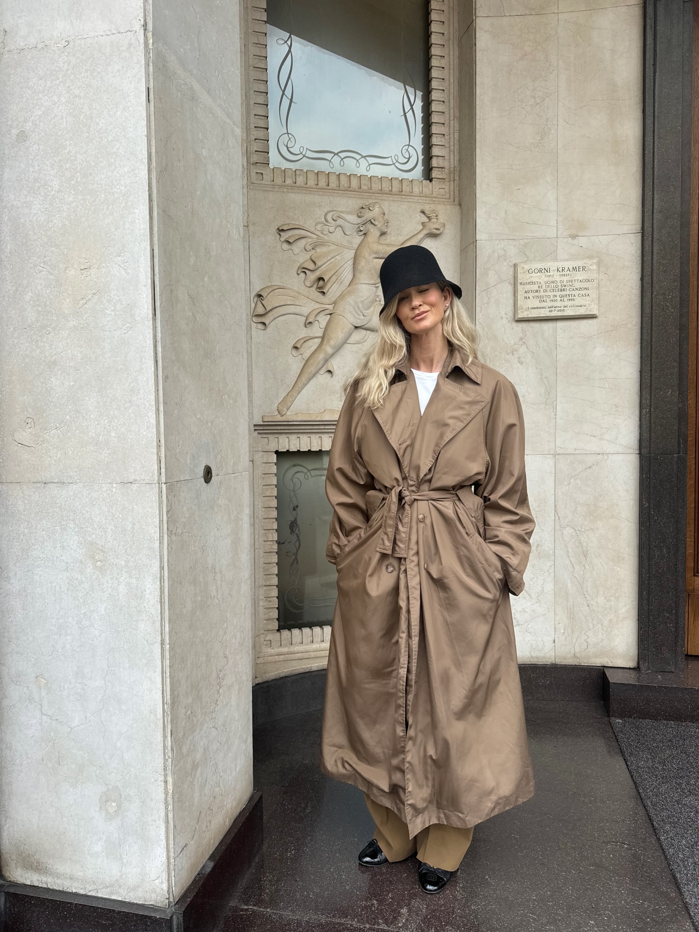 An image of @josefinehj wearing a rich-looking airport outfit including a trench coat, white t-shirt and pleated trousers.