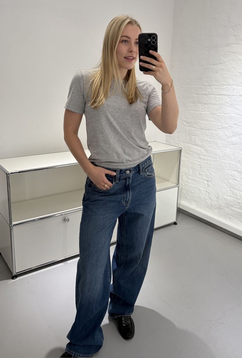 Woman wears grey tee, blue jeans and black loafers