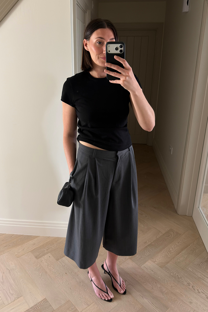 a woman wearing a black baby tee, gray long shorts, and black sandals