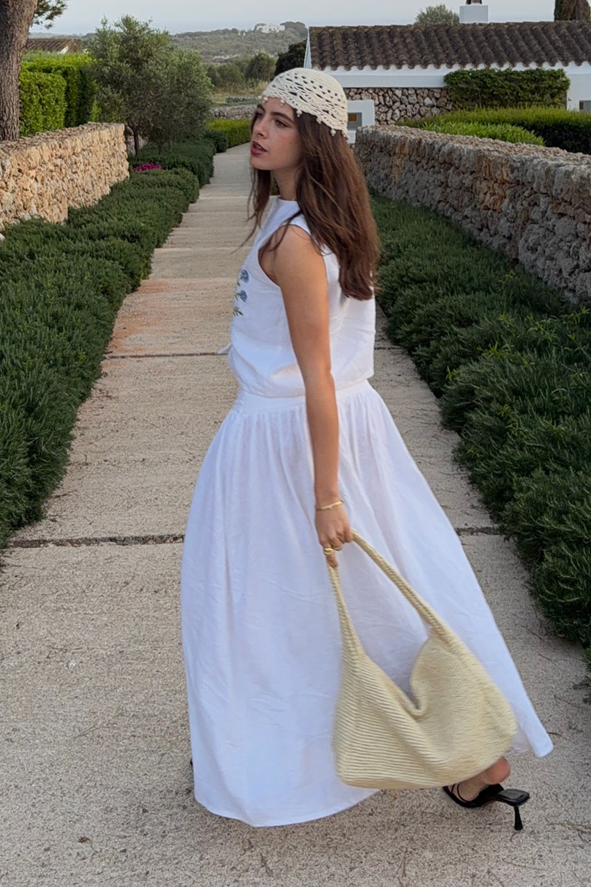 a woman wearing a white dress, cream bag, and crochet skull cap