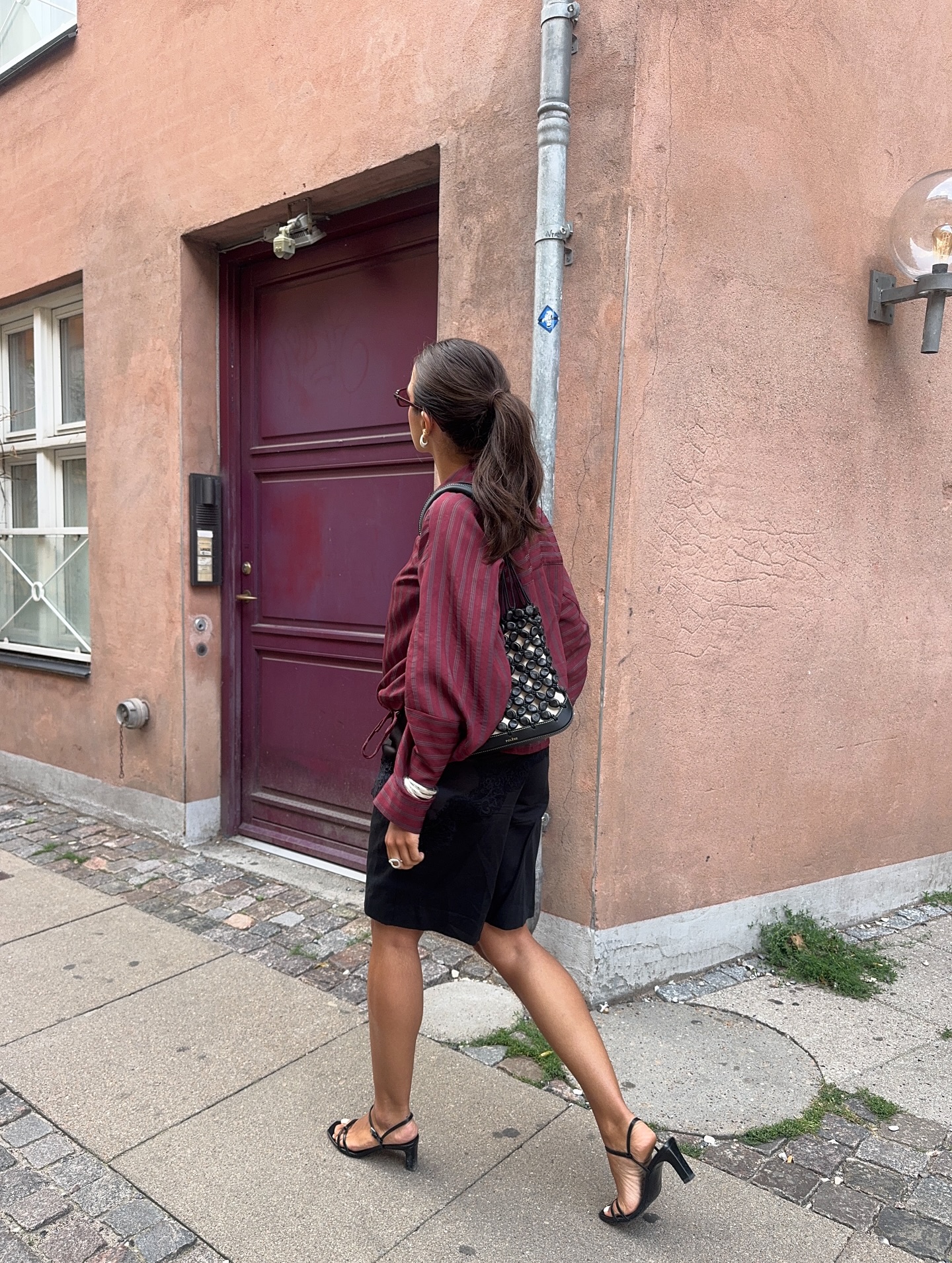 An image of an influencer in Bermuda shorts, striped maroon top and black heels in Copenhgaen