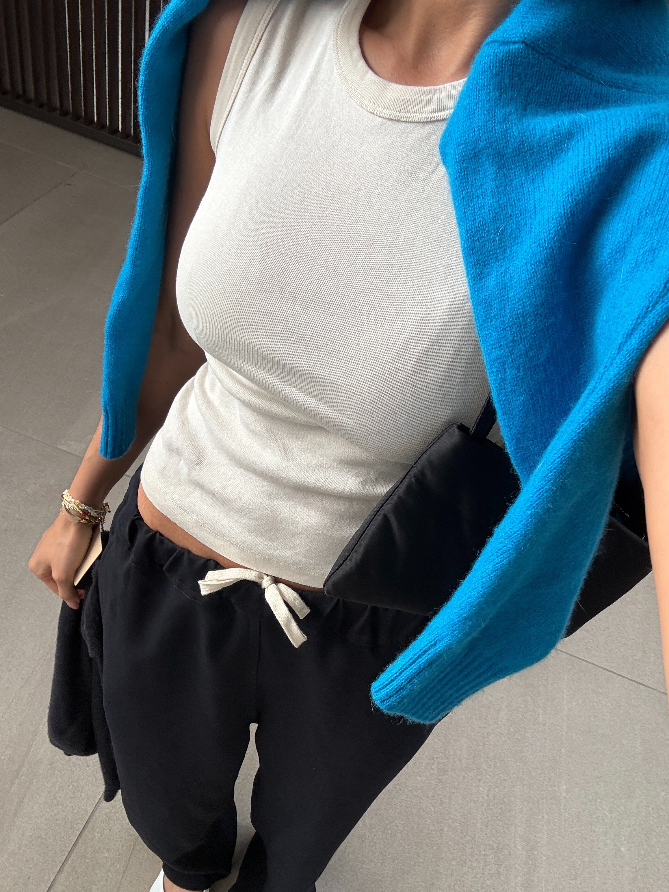 Woman wearing a white tee, sweats, and a colorful sweater around her shoulders.