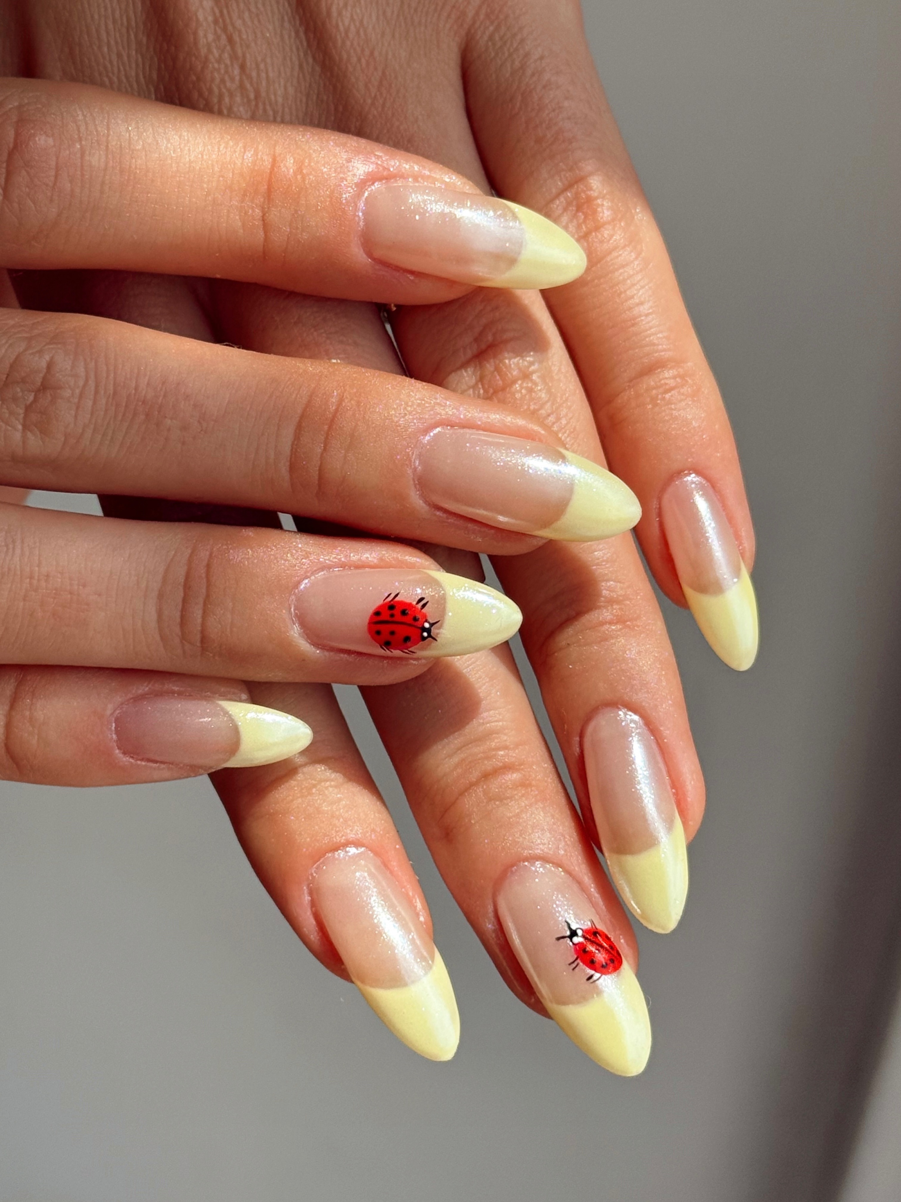 A butter yellow French tip manicure with ladybird nail art