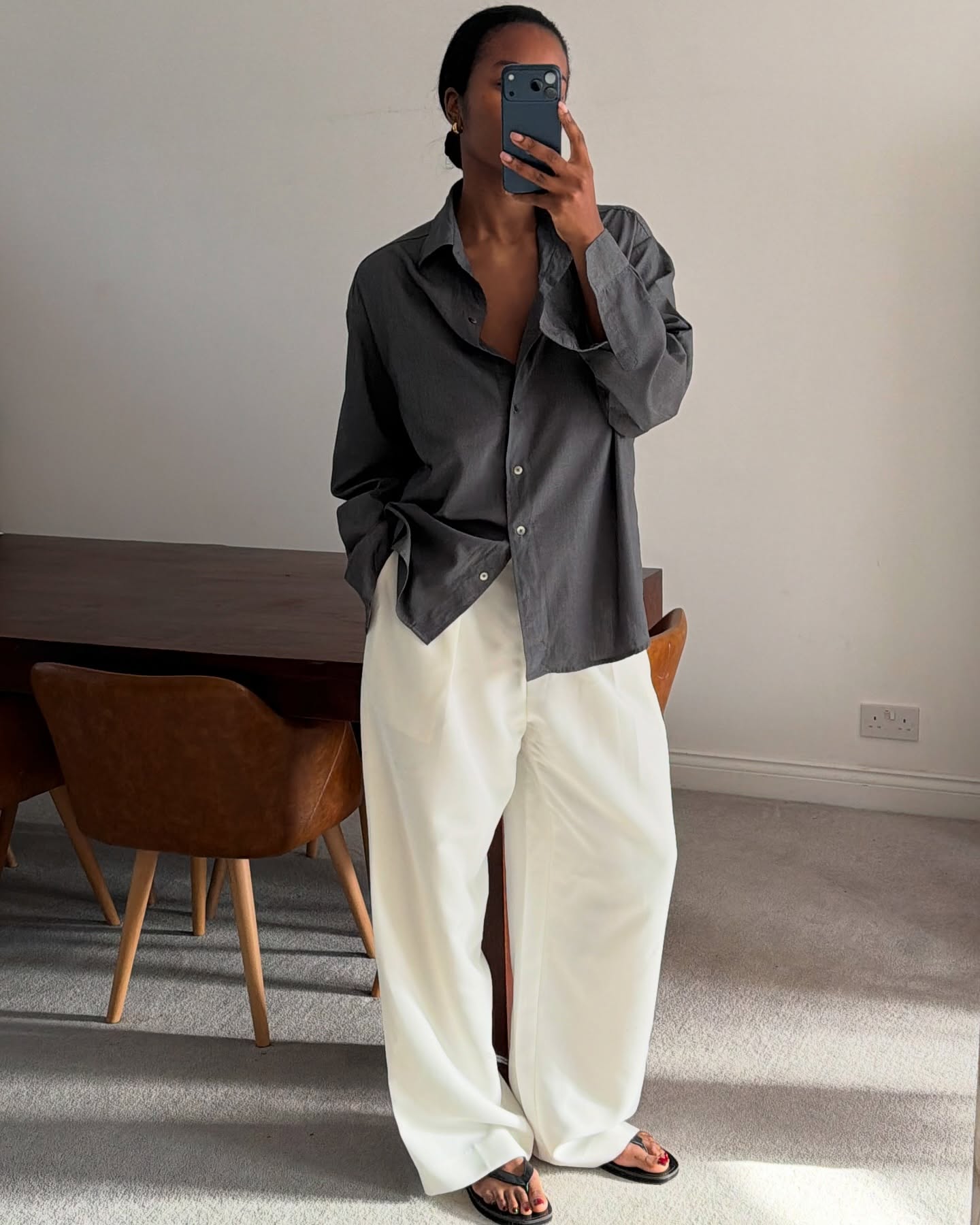 An image of @nlmarilyn wearing a rich-looking airport outfit including a grey shirt, white jeans and black flip-flops.
