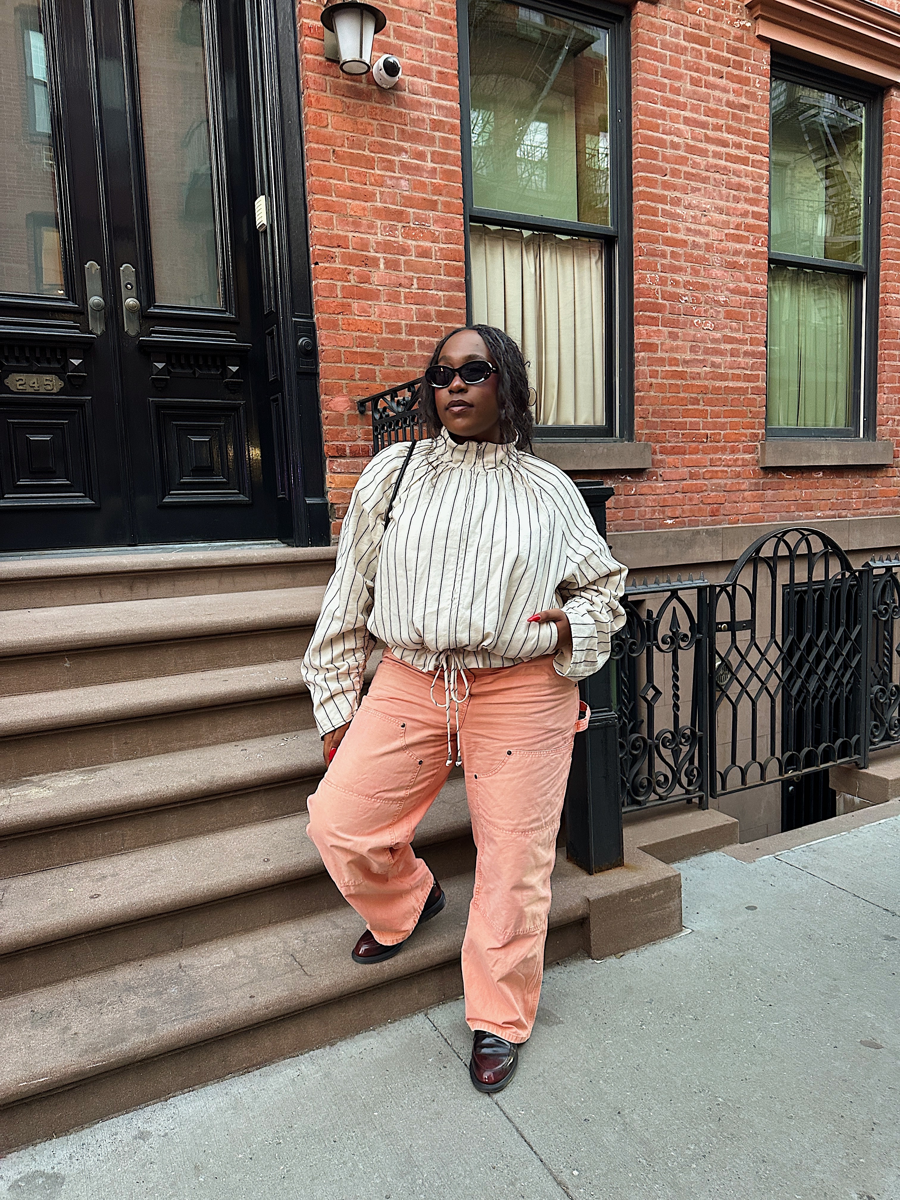 Editor posing in funnel jacket and peach pants on a stoop