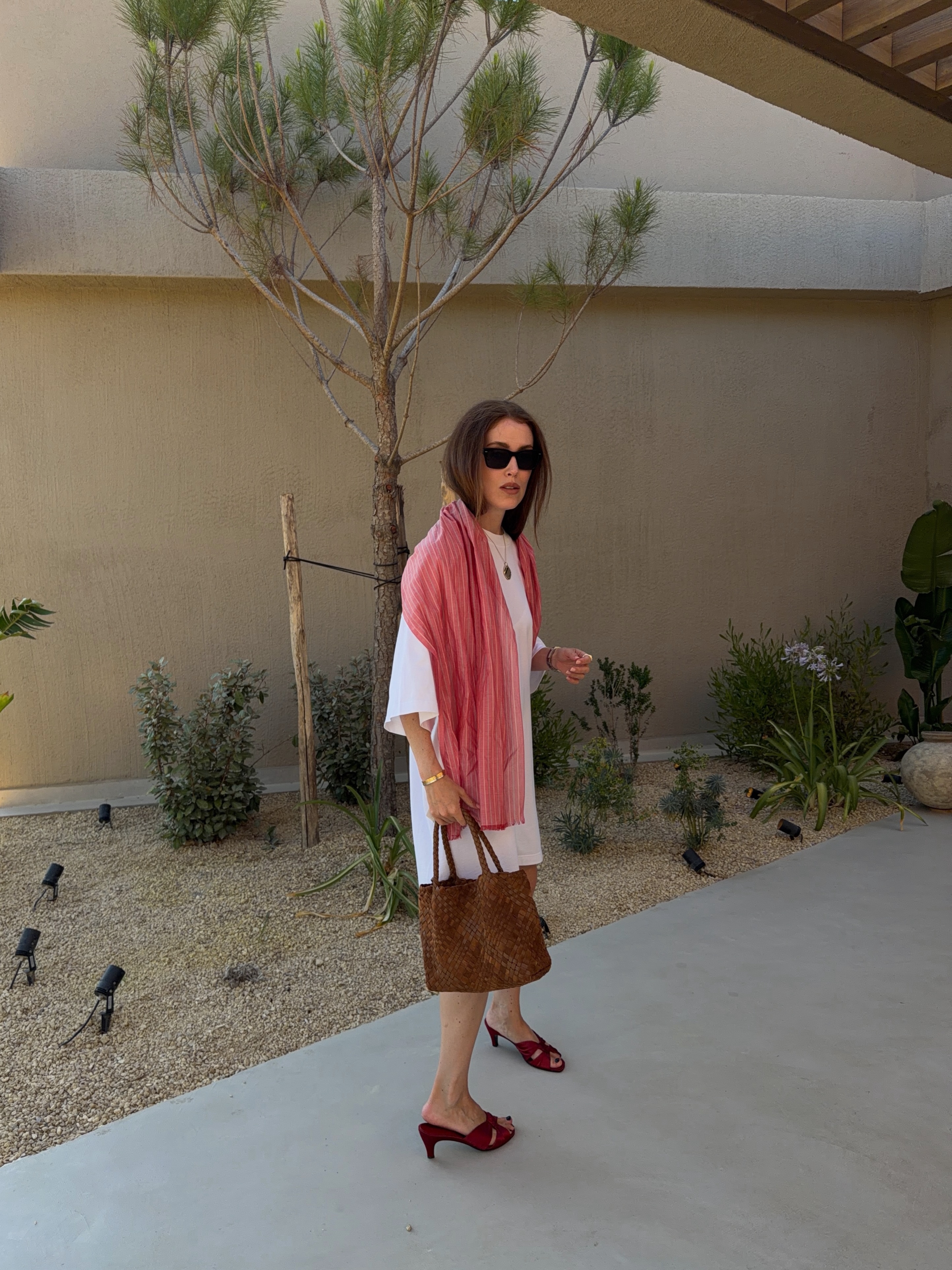 An image of @annabelrosendahl wearing a white t-shirt dress with heeled mules, a suede bag and scarf.