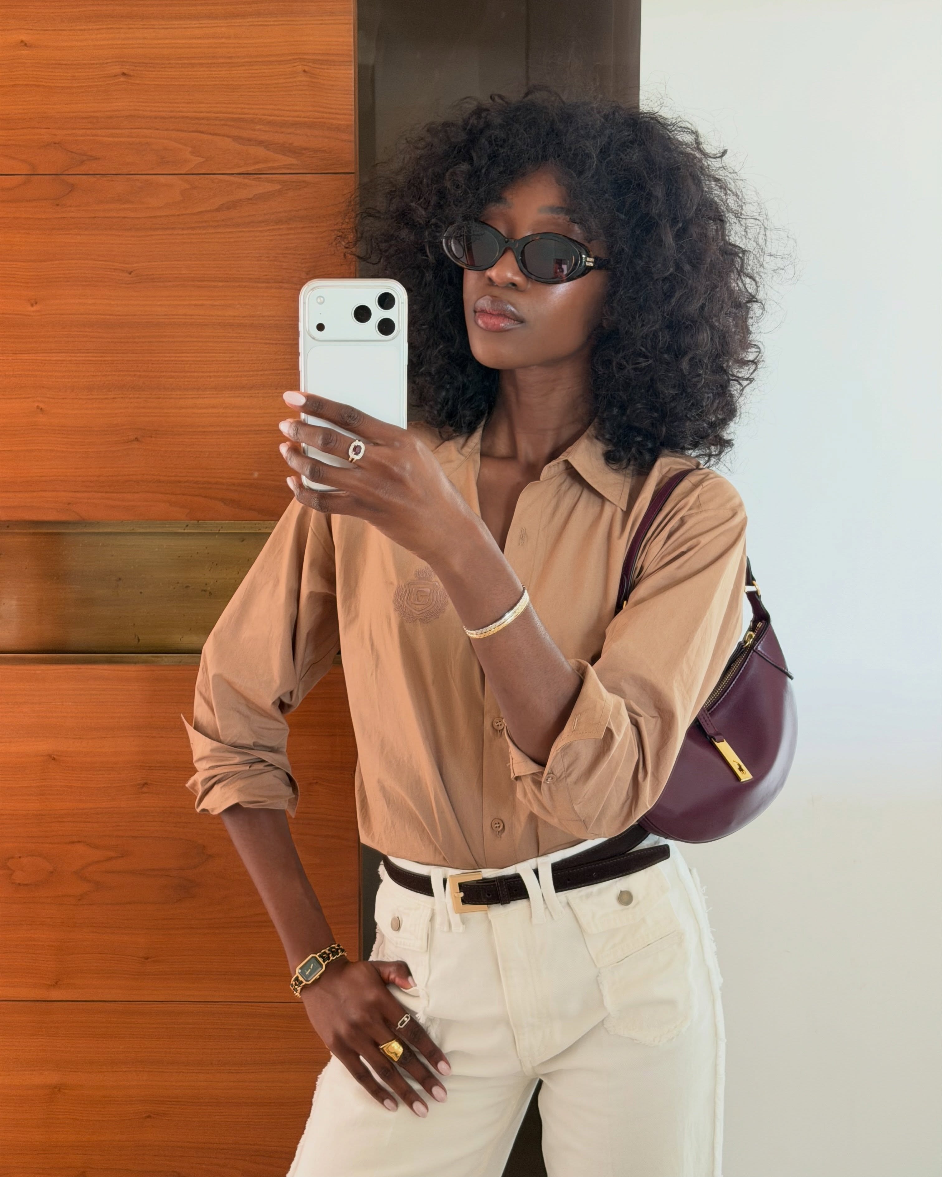 A woman taking a mirror selfie with dark brown, curly hair