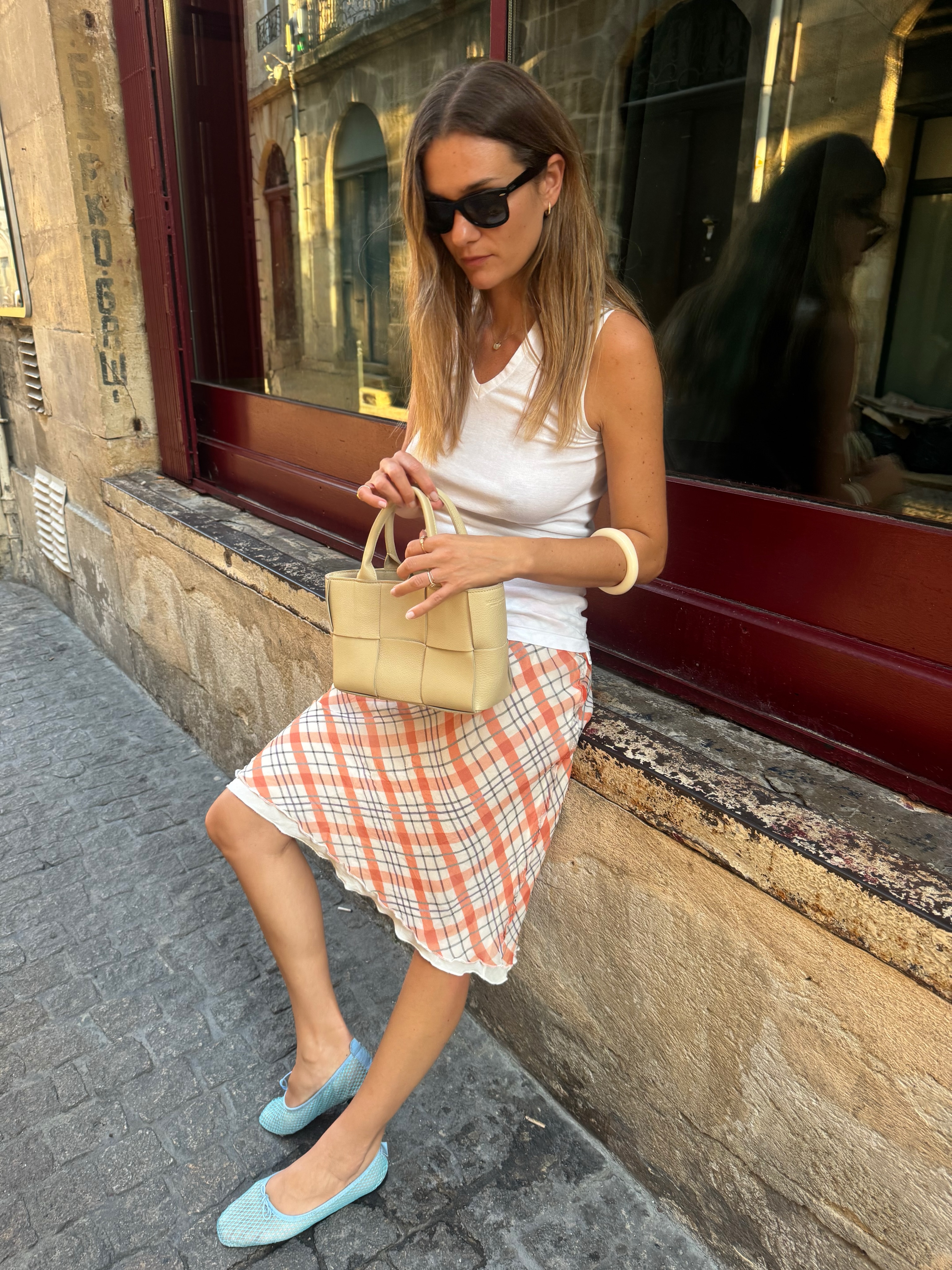 An image of @annelauremais wearing a Realisation Park checked skirt with a white tank top, blue ballet flats and a Bottega Veneta bag.