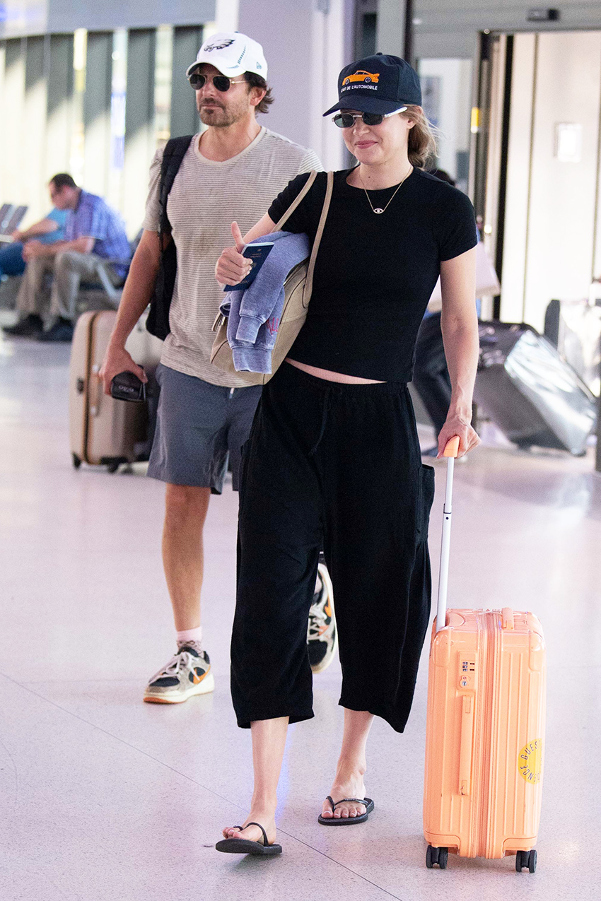 Gigi Hadid wearing a black T-shirt with cropped cargo pants and flip-flops at the airport with Bradley Cooper
