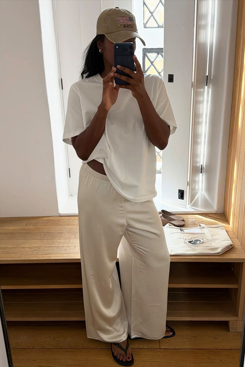 a woman wearing a white tee, white satin pants, and flip-flops