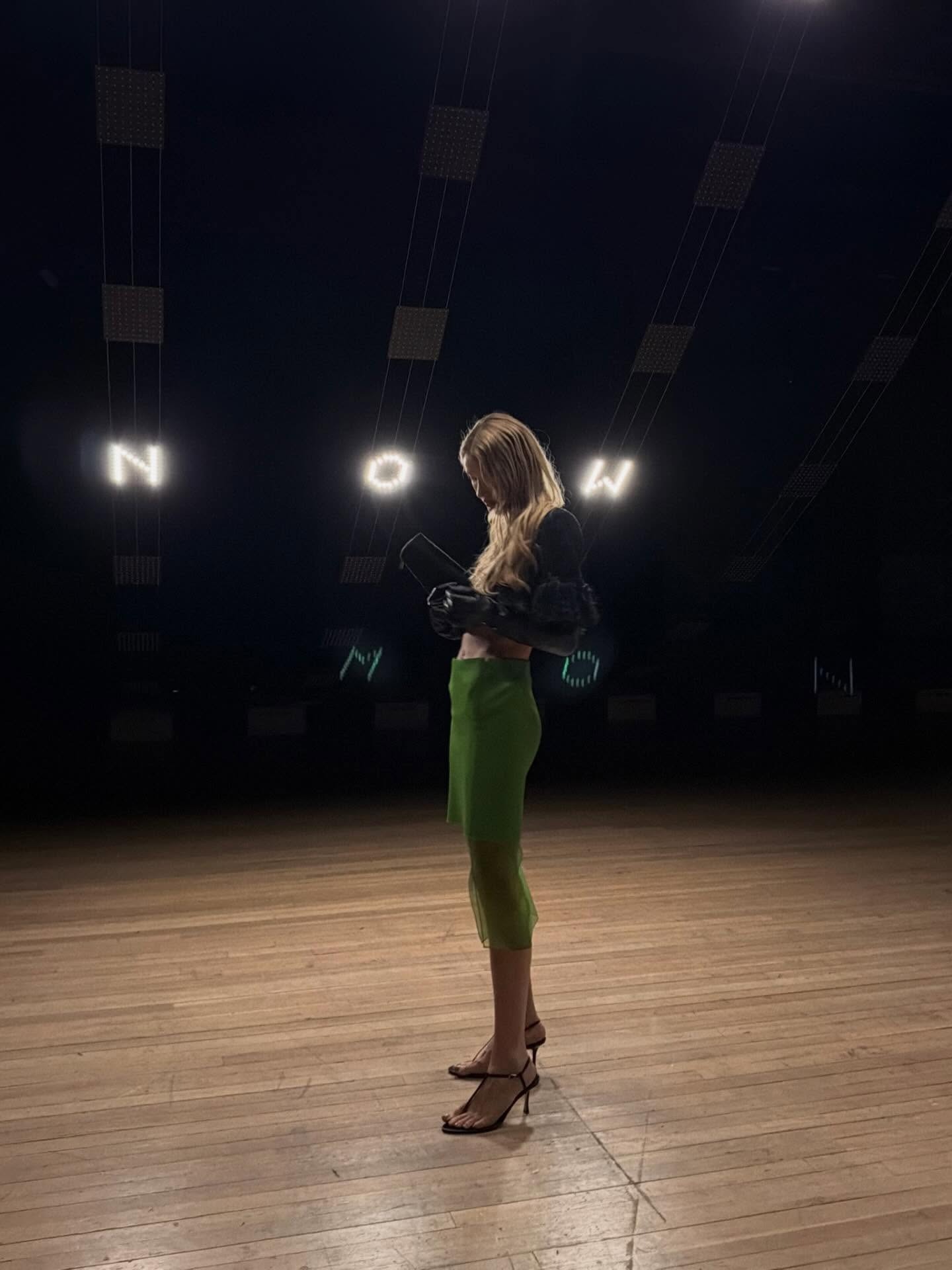 Courtney Grow wearing a crop top, green skirt, and barely-there sandals.