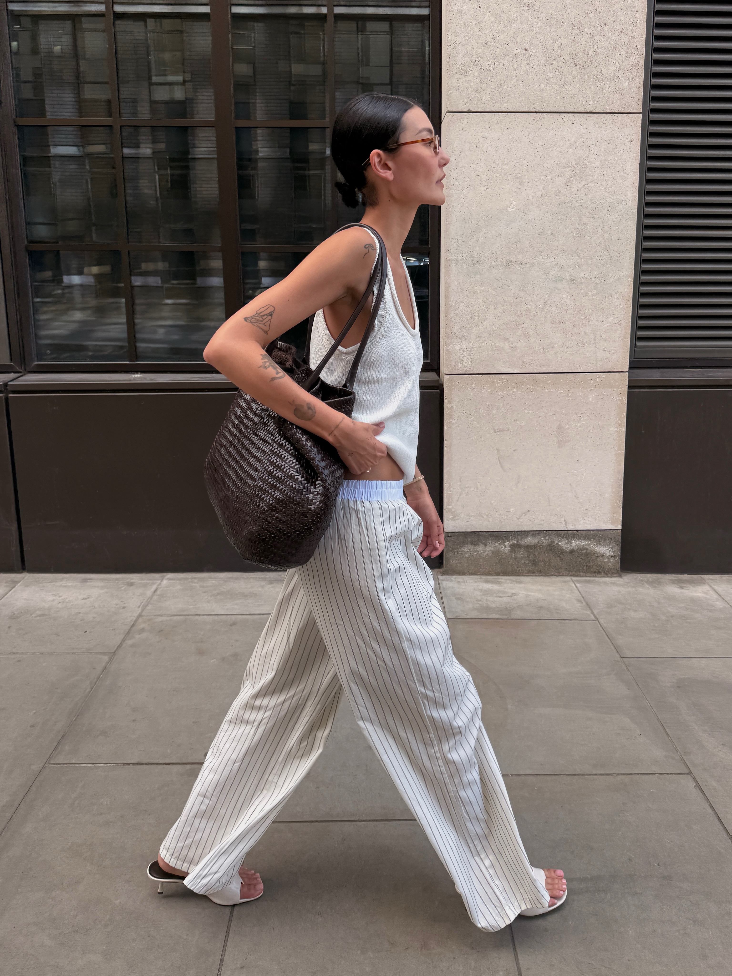 An image of an influencer walking in london wearing a white vest, striped white cotton poplin trousers and white heeled sandals