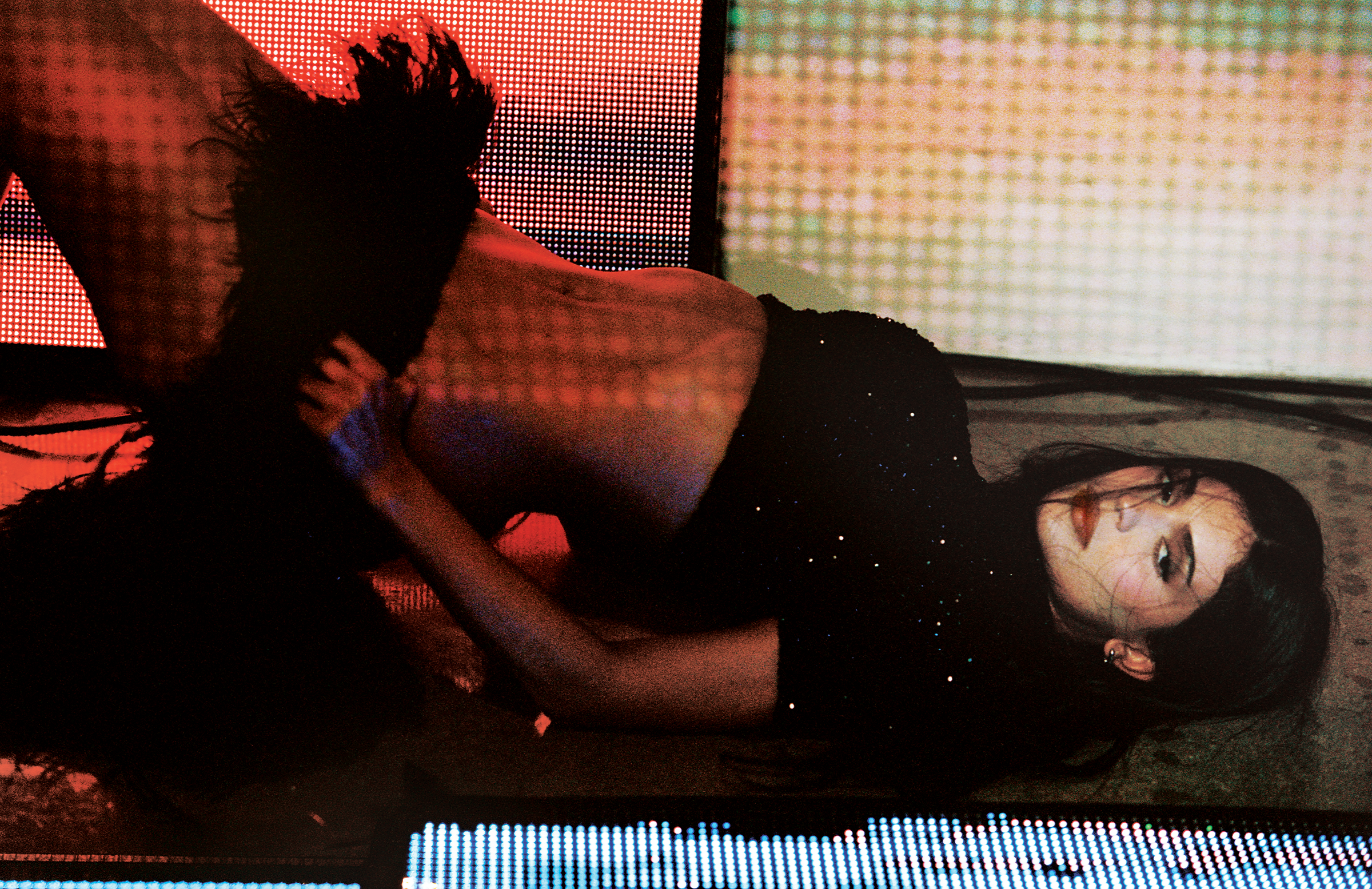 Kylie Jenner wears a black crop top and feather skirt, lying on the ground with images projected on her face and body.