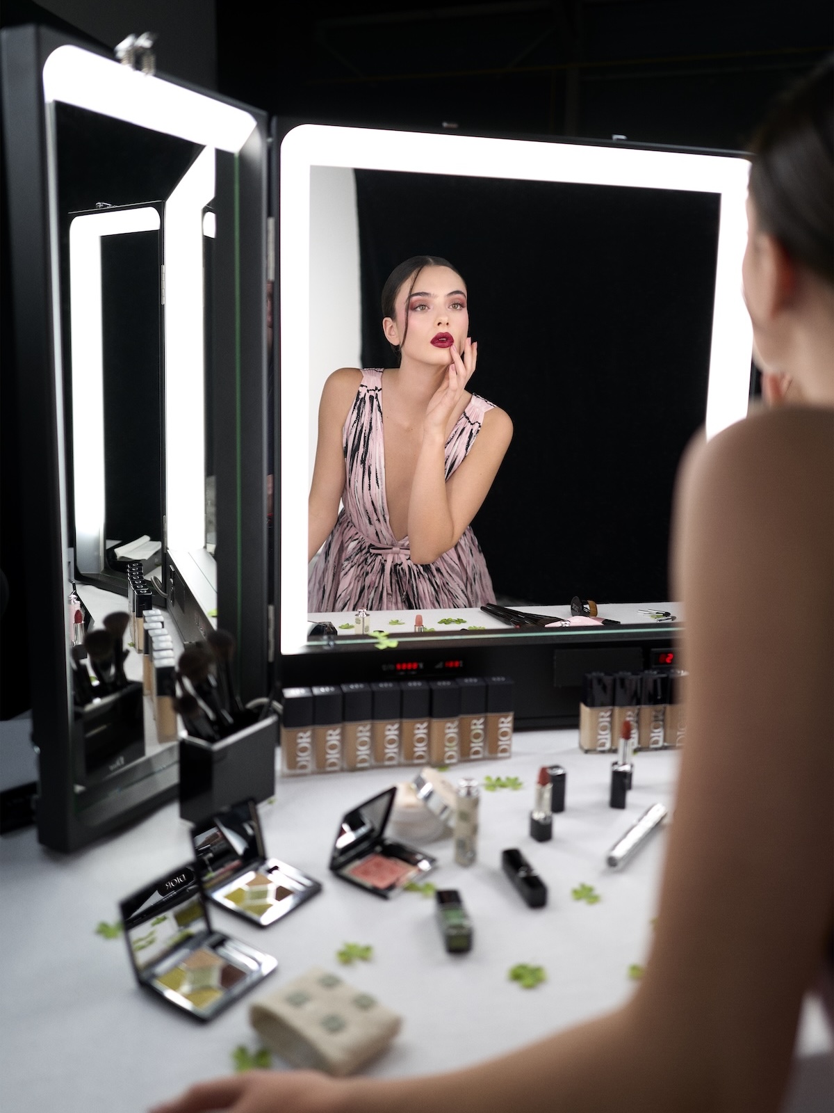 Deva Cassel touching up her makeup in front of a vanity covered in Dior's 