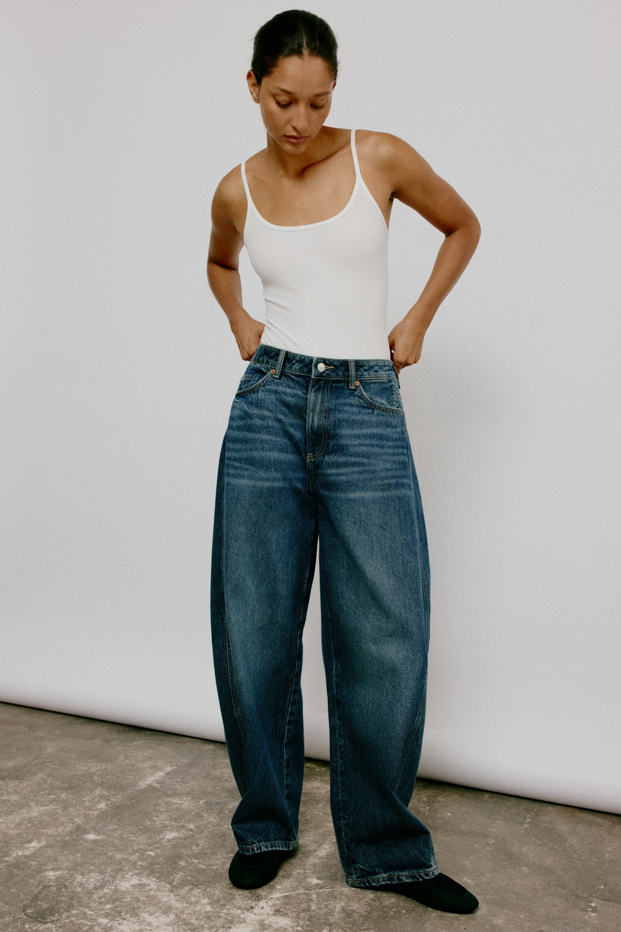 A model wearing a tank top and blue barrel-leg jeans.