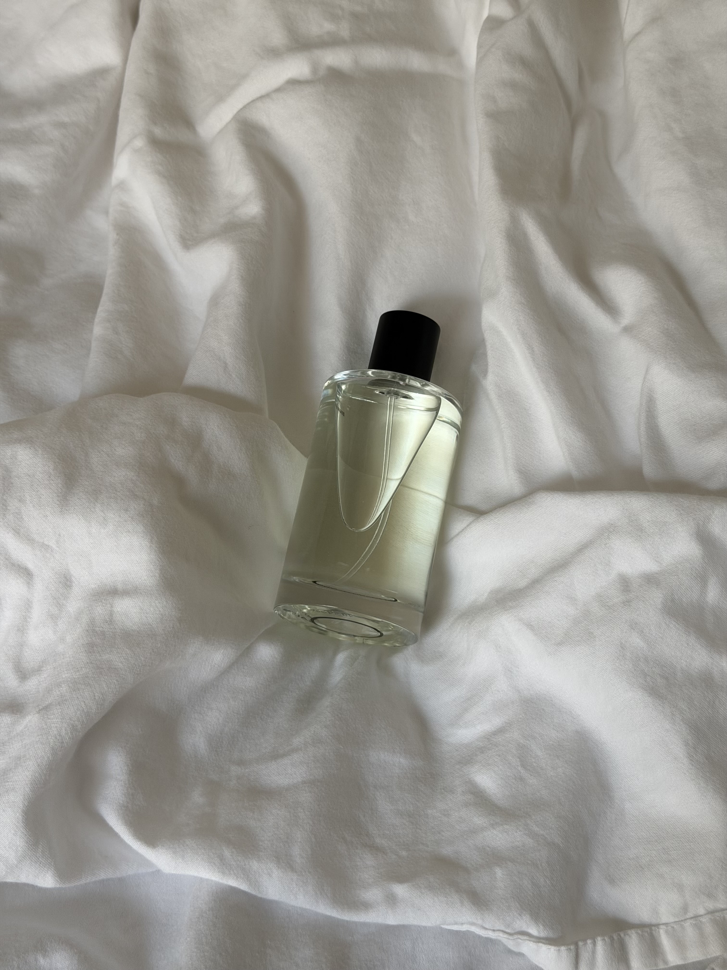 A fragrance bottle on rumpled sheets.